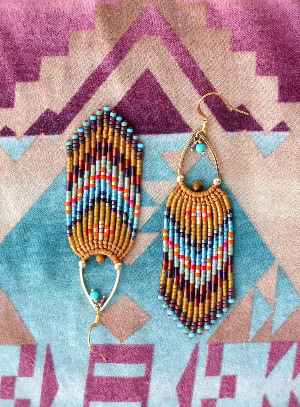 Peut inclure: Paire de boucles d'oreilles faites à la main avec un design bohème. Elles présentent des perles marron, orange, bleues et turquoise disposées verticalement. Les crochets d'oreilles dorés et une perle turquoise ajoutent une touche d'originalité.