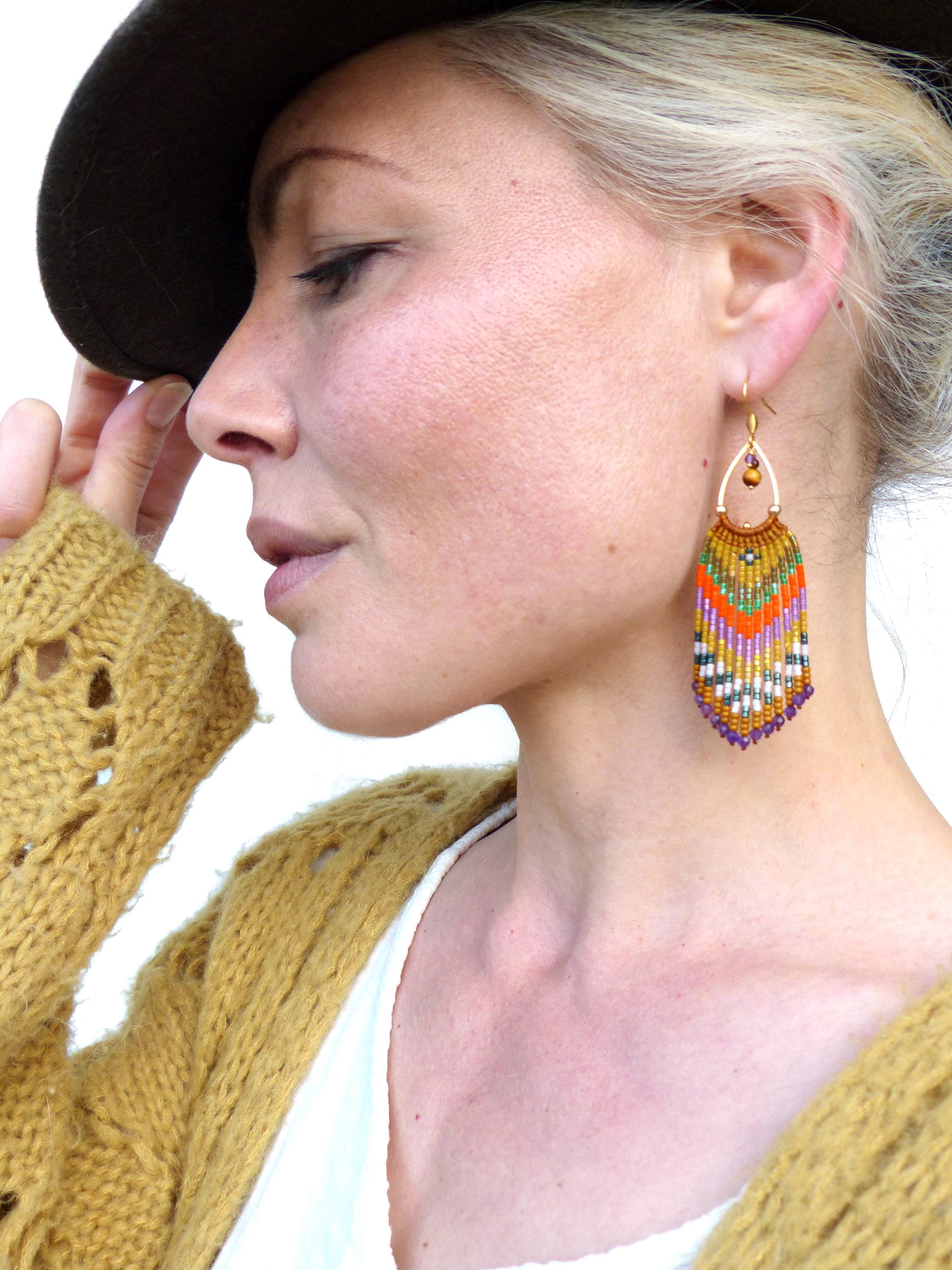Peut inclure: Une paire de longues boucles d'oreilles pendantes en perles de forme goutte d'eau. Les boucles d'oreilles sont faites avec une variété de perles colorées, notamment du violet, de l'orange, du vert et du blanc. Les perles sont disposées selon un motif géométrique, et les boucles d'oreilles sont terminées par un crochet doré.