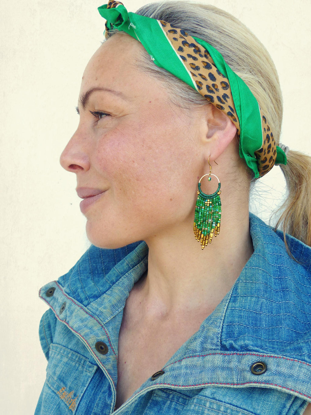 Peut inclure: Une femme portant un foulard à imprimé léopard vert et marron et une veste en jean. Elle porte de longues boucles d'oreilles en perles vertes et dorées.