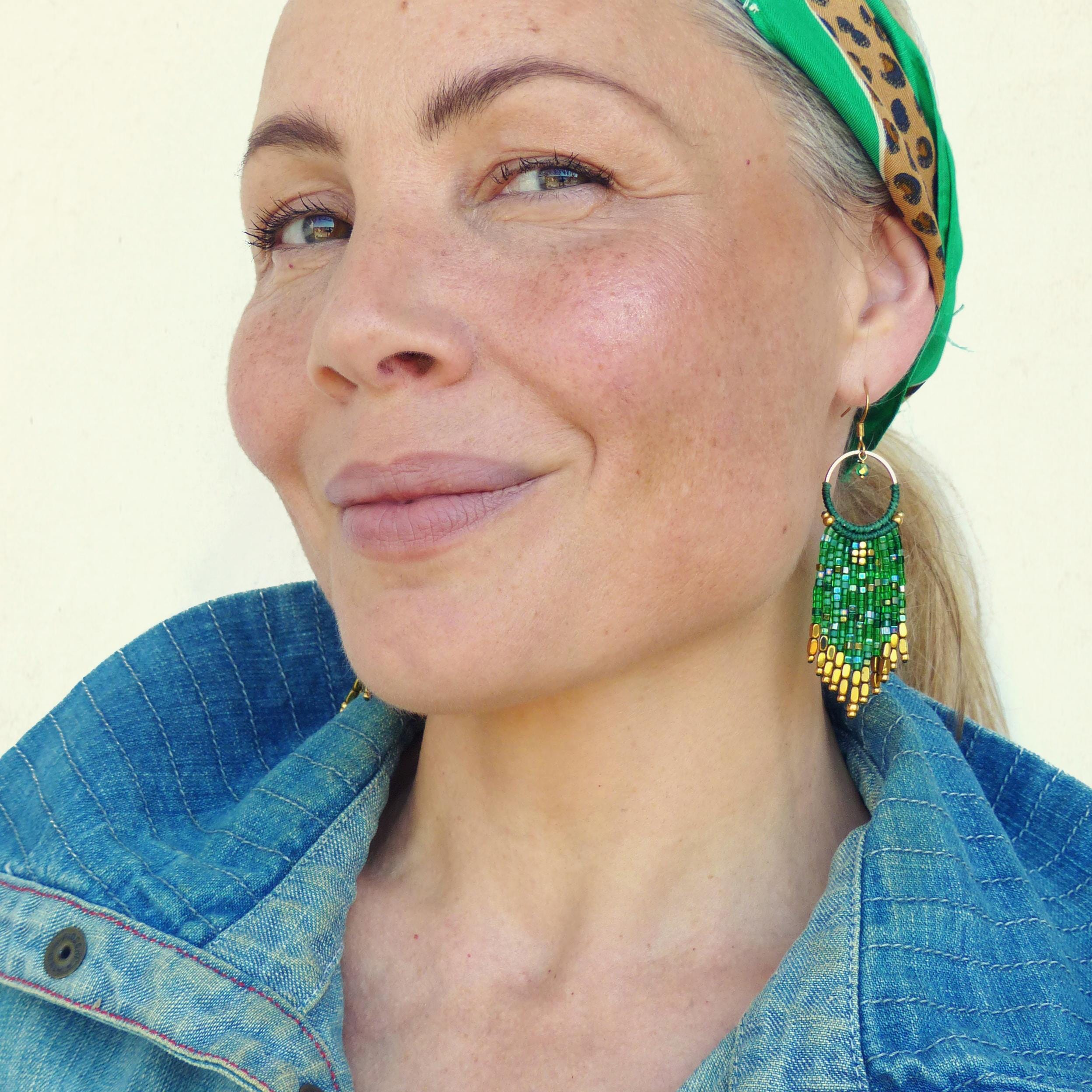 Peut inclure: Une femme portant des boucles d'oreilles à franges en perles vertes et dorées. Les boucles d'oreilles sont longues et pendent de ses oreilles. Elle porte une veste en jean et un bandeau à imprimé léopard.