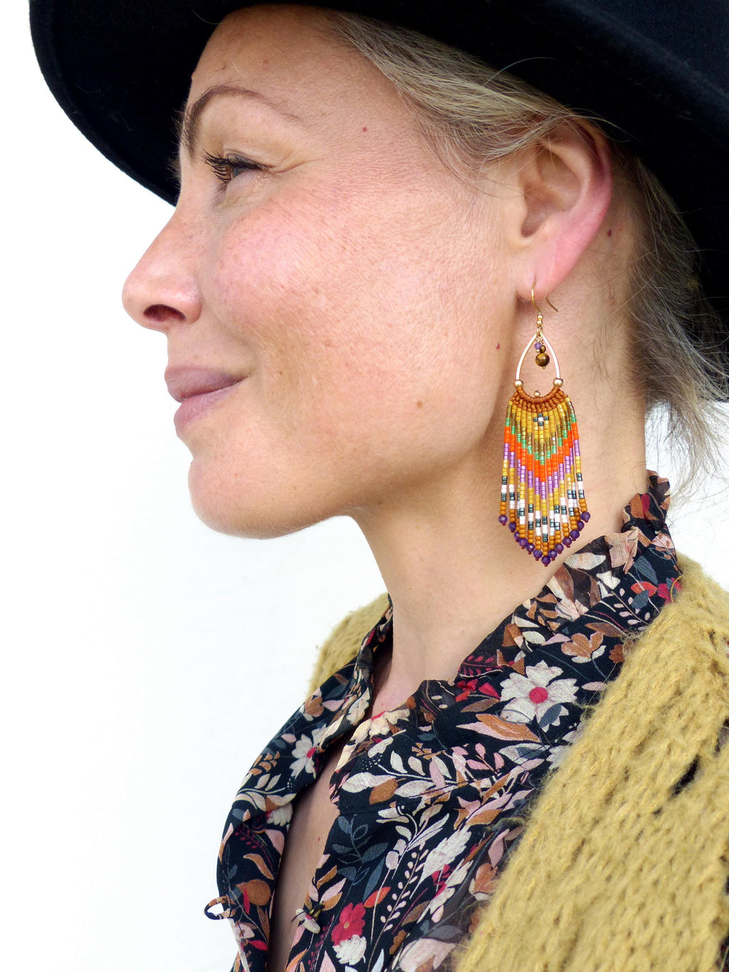 Peut inclure: Une paire de longues boucles d'oreilles en perles colorées avec un crochet doré. Les boucles d'oreilles présentent un motif géométrique avec des perles orange, violettes, blanches et vertes.