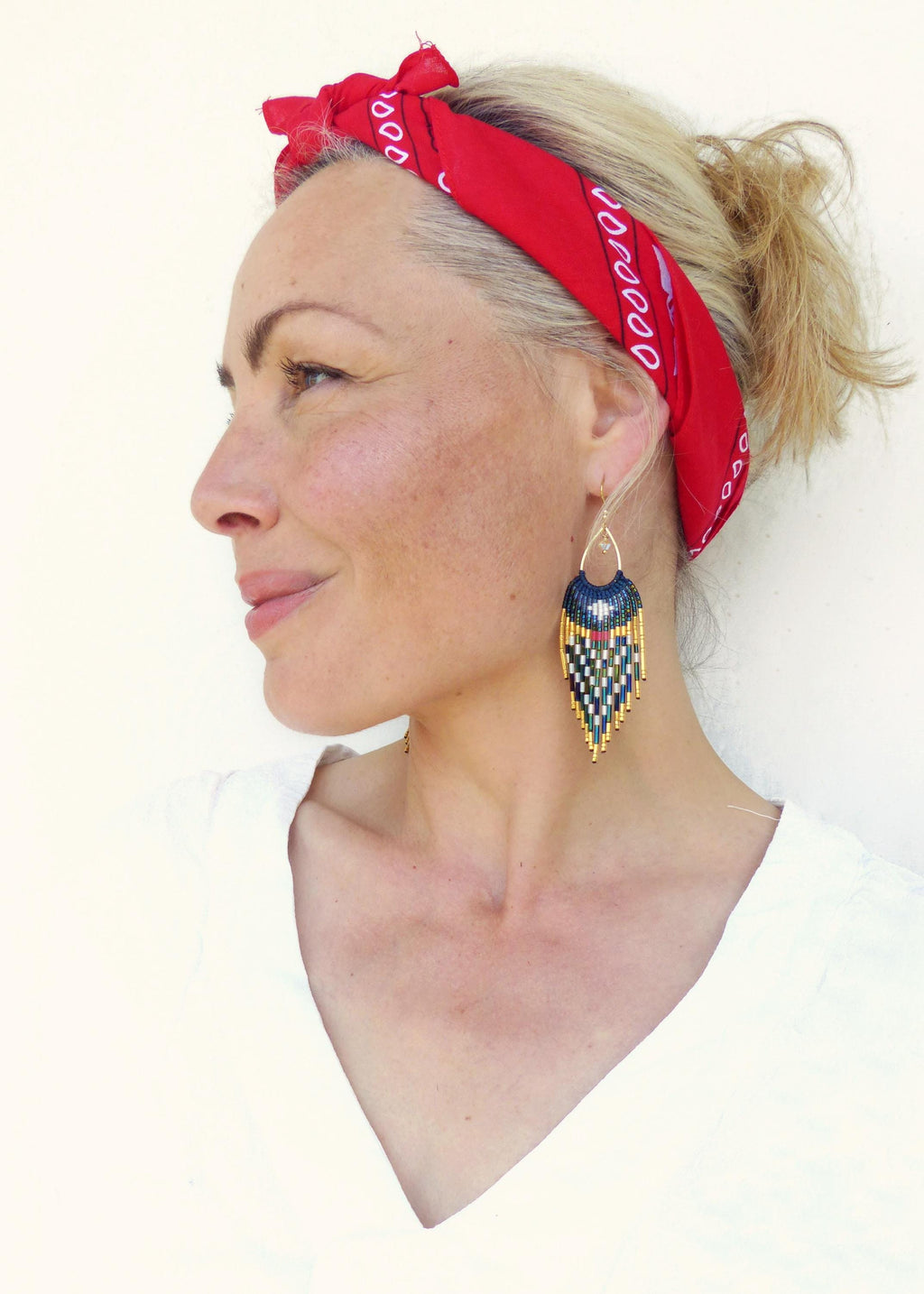 Peut inclure: Boucles d'oreilles dorées avec un motif géométrique perlé en marine, noir, blanc et or. Les boucles d'oreilles ont une forme de goutte d'eau et sont portées avec un bandana rouge.