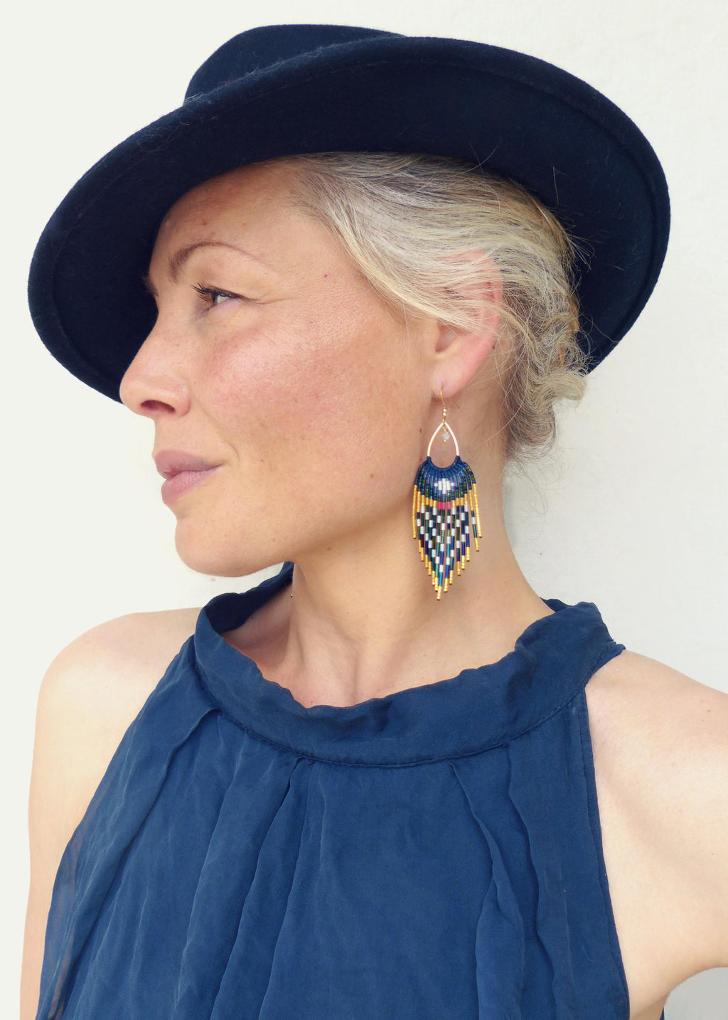 Peut inclure: Une femme porte un chapeau et un haut bleu marine. L'image met l'accent sur une paire de boucles d'oreilles en perles avec un crochet doré. Les boucles d'oreilles présentent un motif géométrique bleu marine, sarcelle, blanc et or.