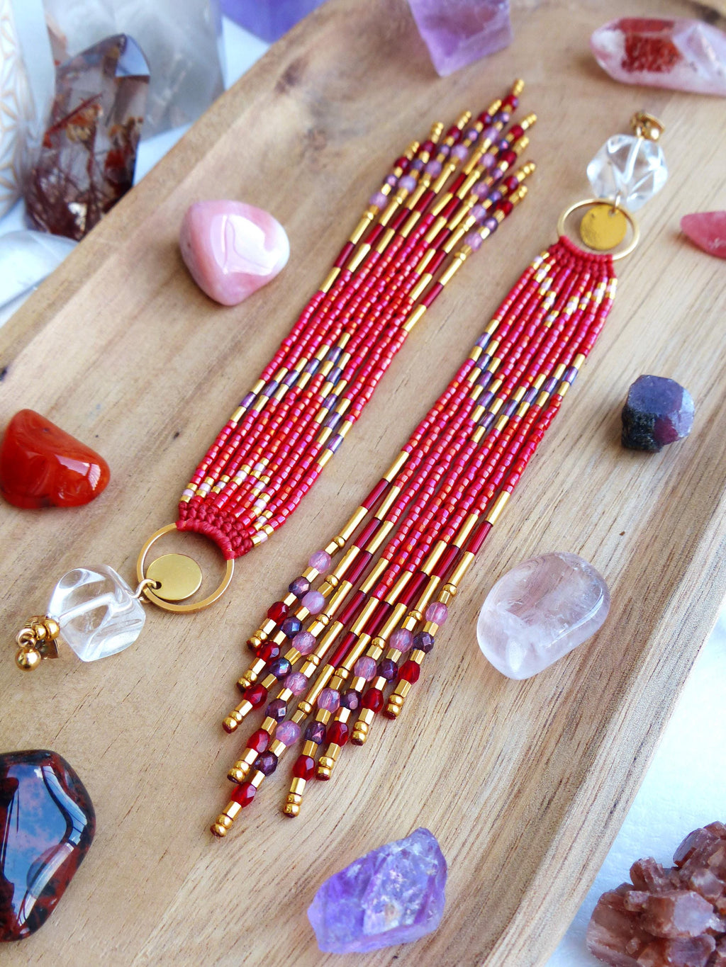 Peut inclure: Boucles d'oreilles rouges faites à la main avec des perles dorées et un design à franges. Les boucles d'oreilles sont présentées sur un plateau en bois avec diverses pierres précieuses, dont du quartz et de l'améthyste. Les boucles d'oreilles mesurent environ 10 cm.