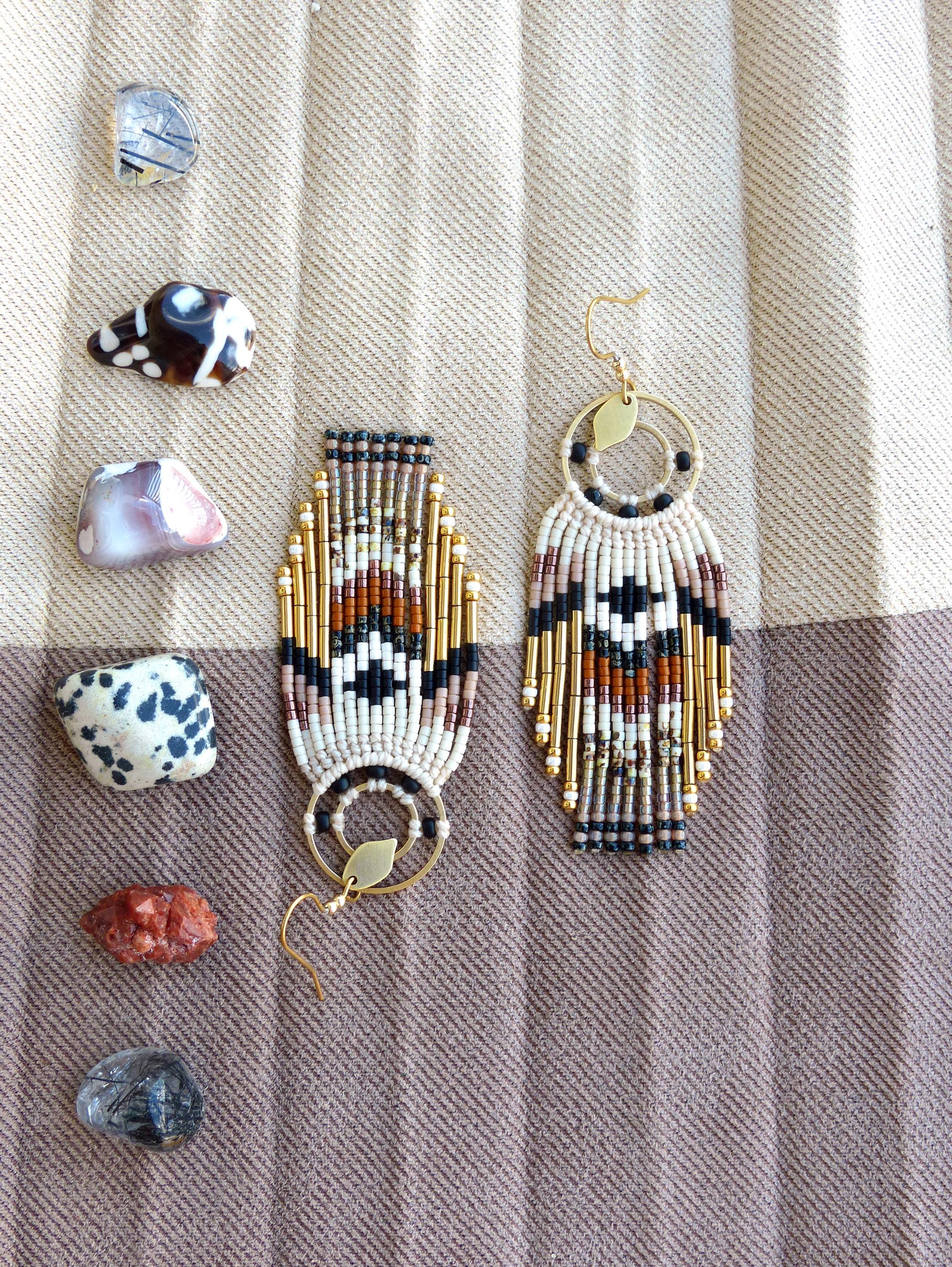 Peut inclure: Boucles d'oreilles faites à la main avec un motif géométrique en noir, blanc, marron et or. Les boucles d'oreilles ont un aspect de frange et sont présentées avec diverses pierres colorées sur un fond en tissu rayé.