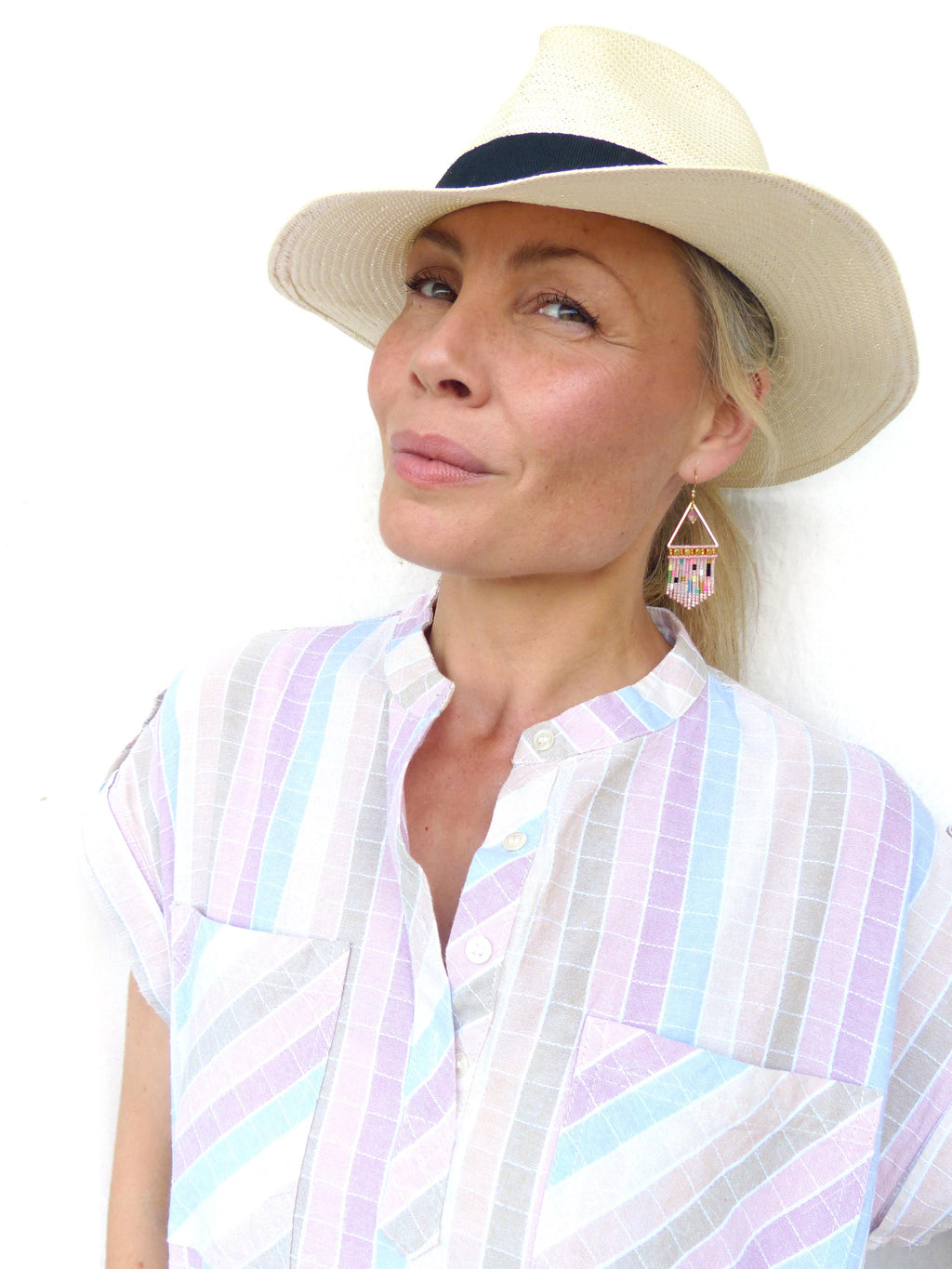 Peut inclure: Un chapeau de paille crème avec un ruban noir et une chemise à rayures pastel. La chemise a un col mandarin et deux poches avant. Les boucles d'oreilles sont géométriques avec des perles roses, bleues et jaunes.