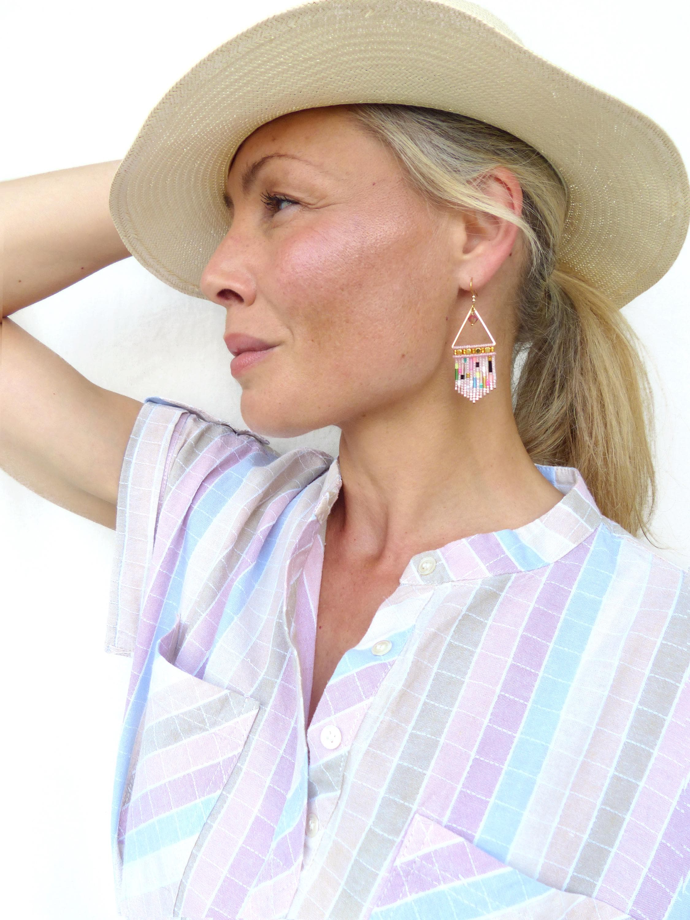 Peut inclure: Une femme porte un chapeau de paille et une chemise à carreaux pastel. La femme porte des boucles d'oreilles géométriques en perles avec des perles roses, blanches et noires. Les boucles d'oreilles sont de forme triangulaire et sont suspendues à des crochets dorés.