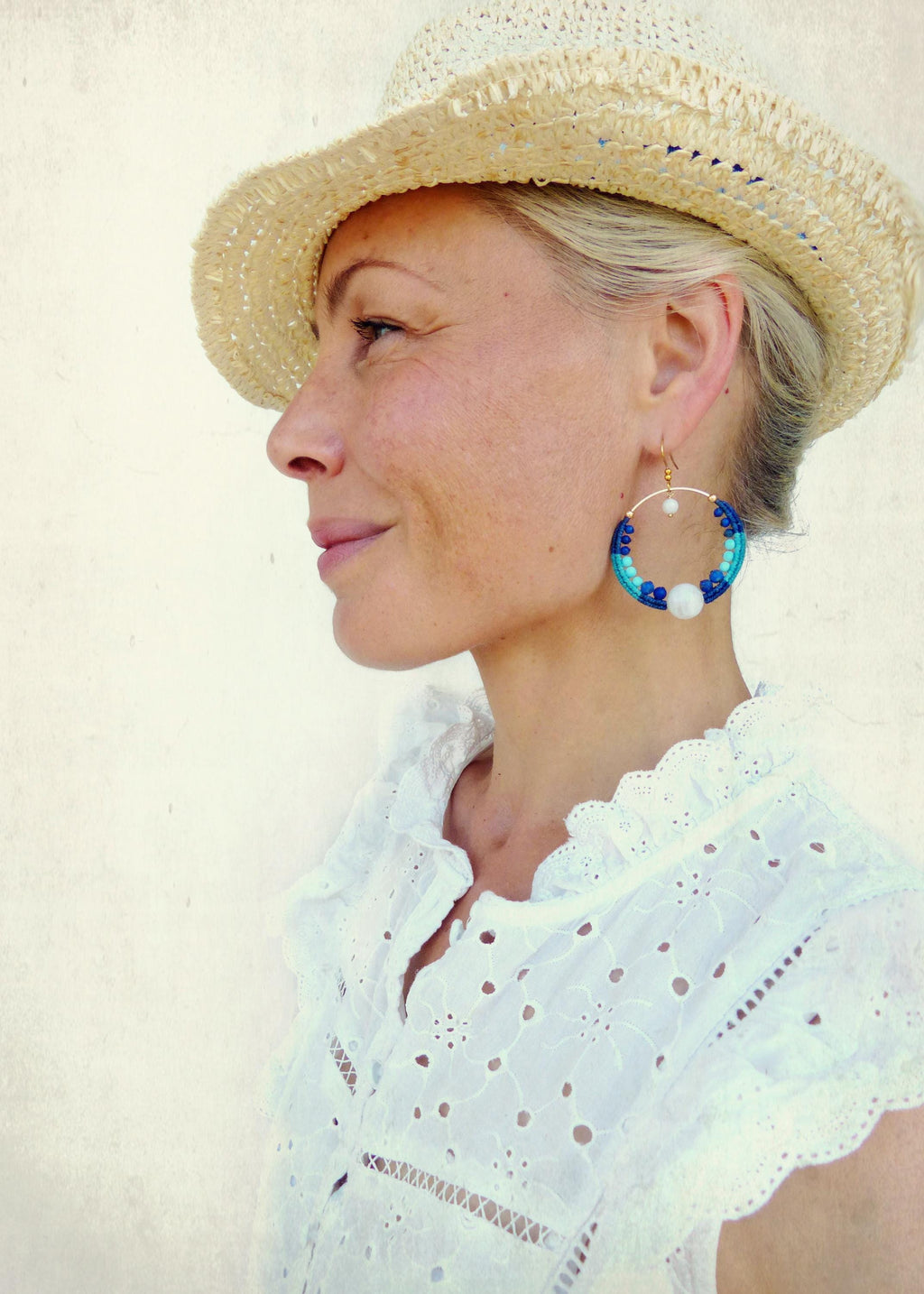 Peut inclure: Une femme porte un chapeau de paille et de grandes boucles d'oreilles créoles. Les boucles d'oreilles sont dorées avec des perles bleues et blanches. Elle porte un chemisier blanc à œillets. Les boucles d'oreilles mesurent environ 7,6 cm de diamètre.