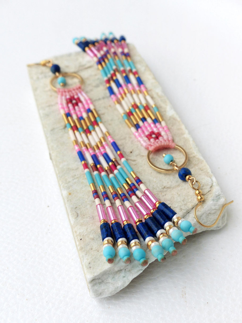 Peut inclure: Boucles d'oreilles perlées faites à la main avec une palette de couleurs vives. Les boucles d'oreilles présentent une combinaison de perles roses, bleues, blanches et dorées, avec un design à franges. Les boucles d'oreilles ont un cerceau doré et une fermeture à crochet.