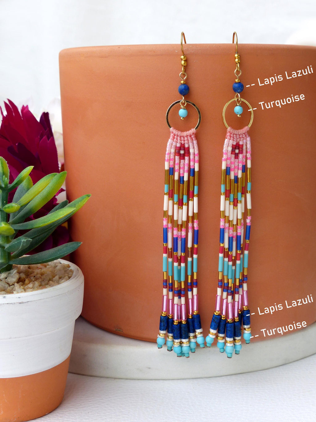 Peut inclure: Longues boucles d'oreilles perlées avec des crochets et des cerceaux dorés. Les boucles d'oreilles présentent un motif de perles roses, bleues, blanches et dorées. Le texte "Lapis Lazuli - Turquoise" est visible sur le côté droit de l'image.
