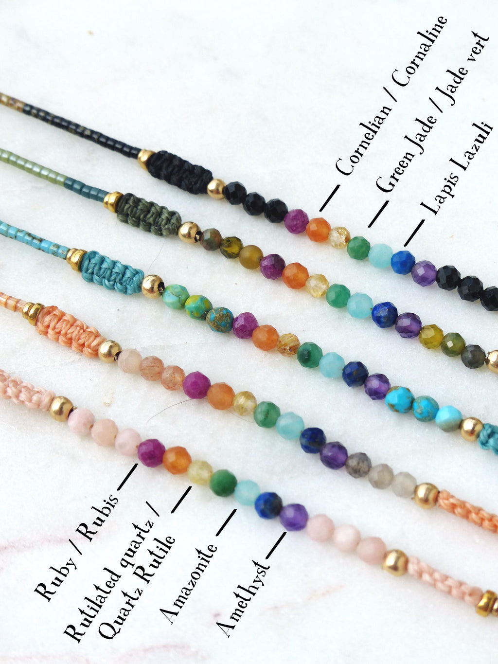 Peut inclure: Gros plan sur cinq bracelets de perles avec diverses pierres précieuses, dont le rubis, l'améthyste et le jade vert. Chaque bracelet présente une palette de couleurs différente et est enfilé sur un cordon avec des accents dorés. Les noms des pierres sont indiqués.
