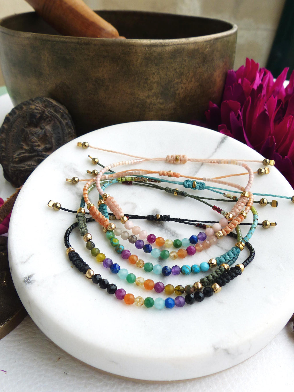 Peut inclure: Plusieurs bracelets de perles de différentes couleurs, dont le noir, le vert, le bleu, l'orange et le rose. Les bracelets sont présentés sur une surface en marbre blanc. Chaque bracelet comporte de petites perles colorées et des accents dorés.