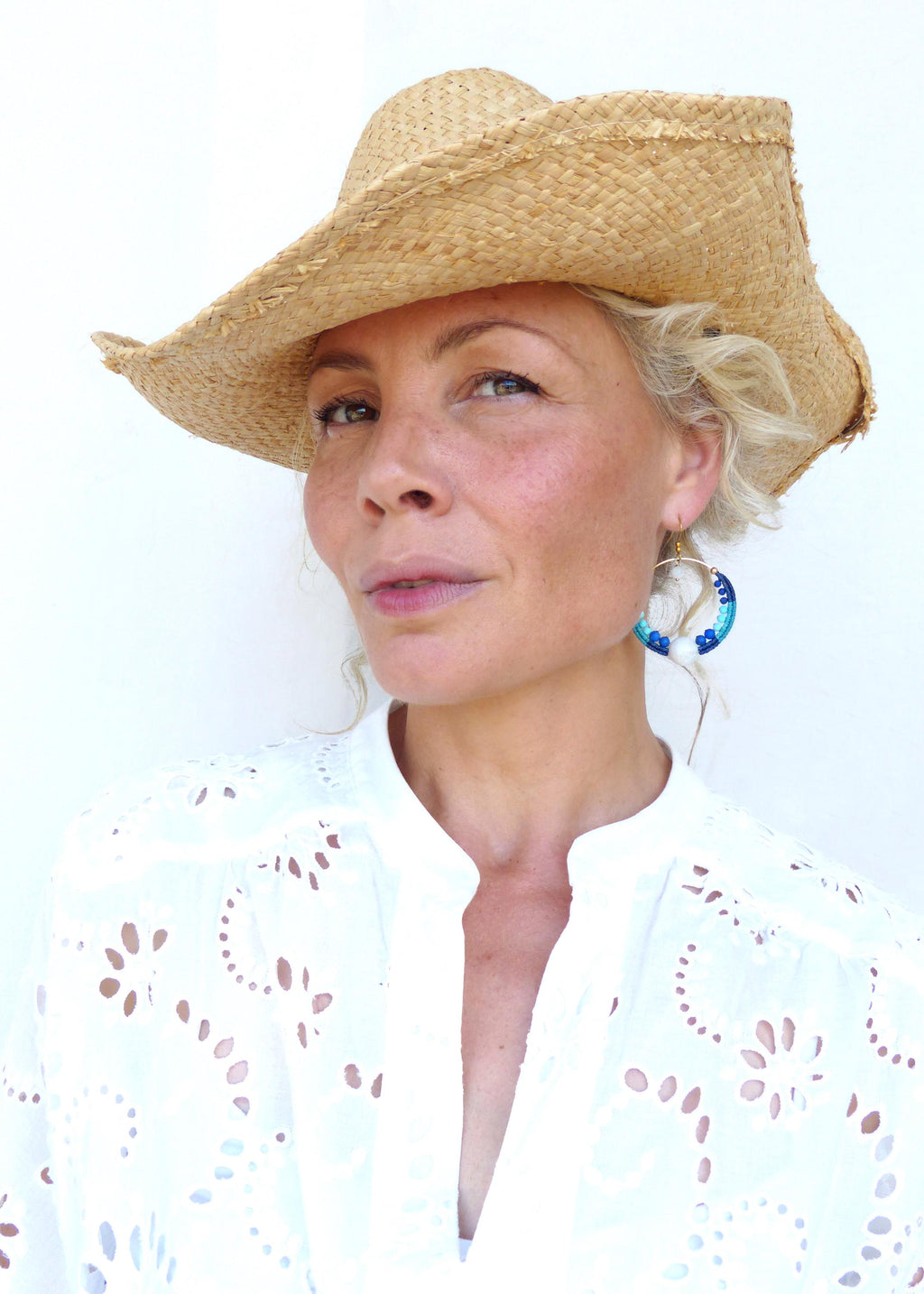 Peut inclure: Un chapeau de paille à larges bords et une chemise blanche à œillets. Les boucles d'oreilles sont des créoles dorées avec des détails bleus et blancs. Le chapeau est en paille tressée.