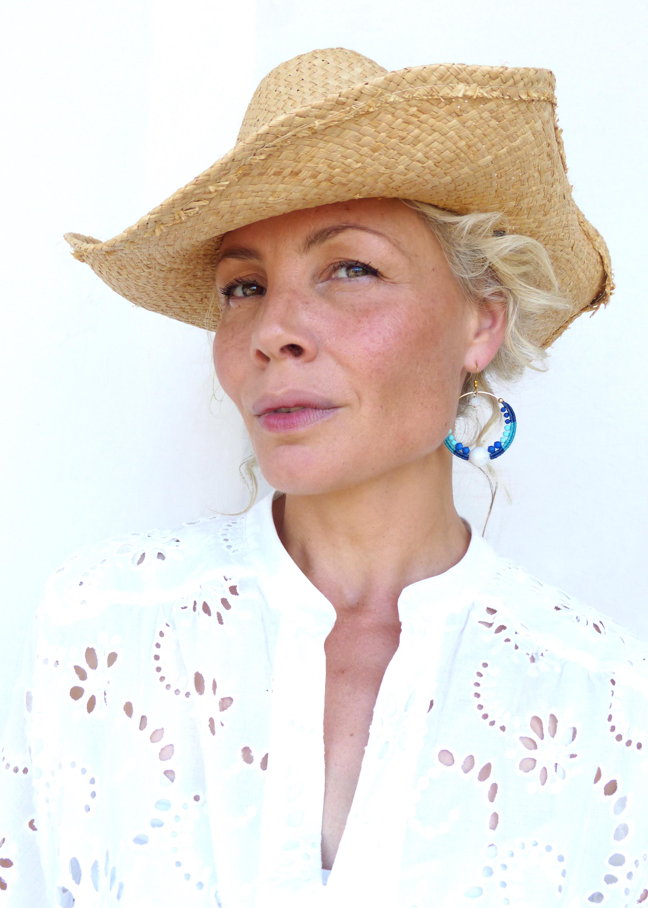 Peut inclure: Un chapeau de paille à larges bords et une chemise blanche à œillets. Les boucles d'oreilles sont des créoles dorées avec des détails bleus et blancs. Le chapeau est en paille tressée.