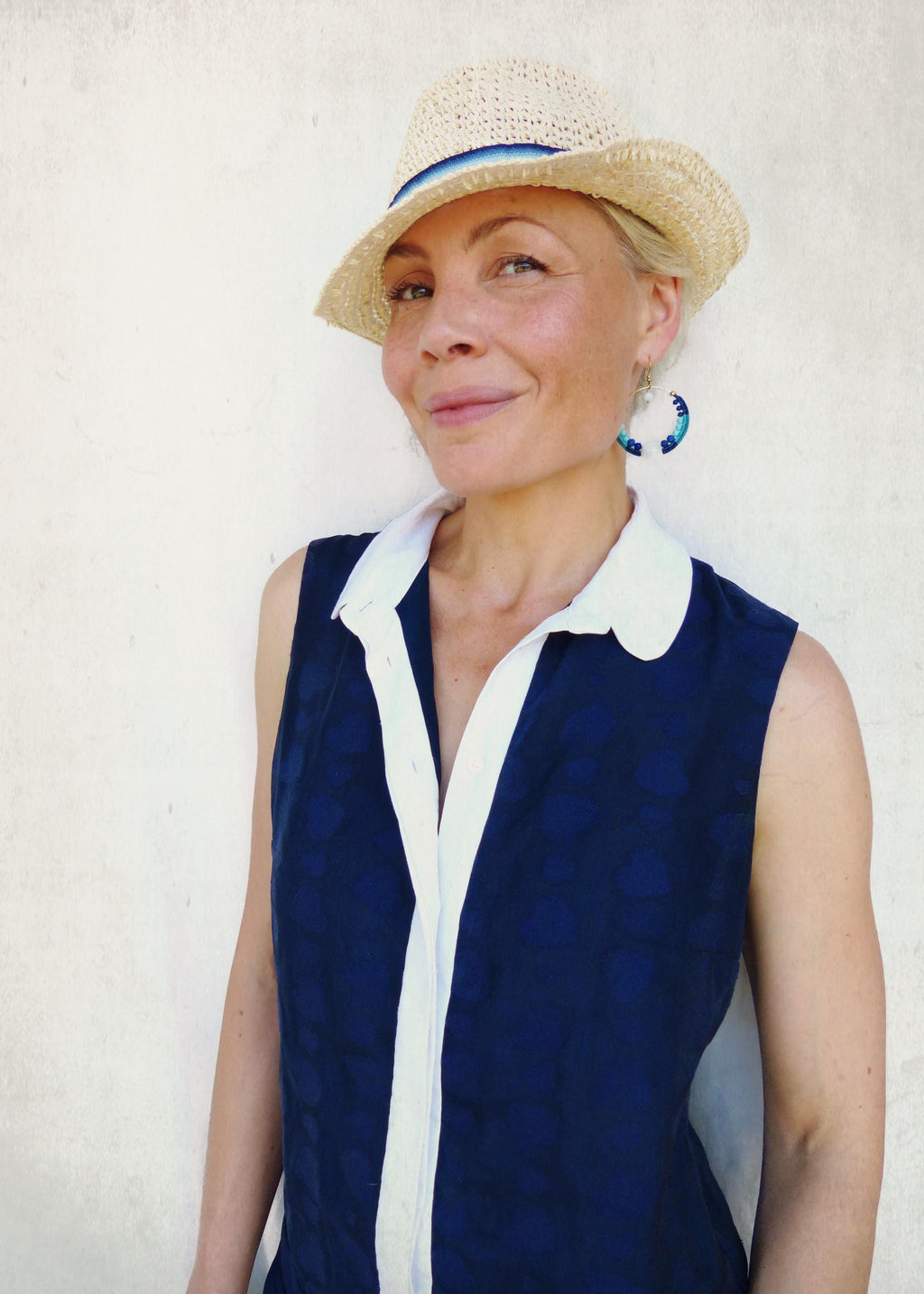 Peut inclure: Un chapeau de paille avec un ruban bleu et un haut sans manches bleu marine avec un col et une bordure blancs. Le haut a un motif subtil. La personne porte des boucles d'oreilles bleues et blanches.
