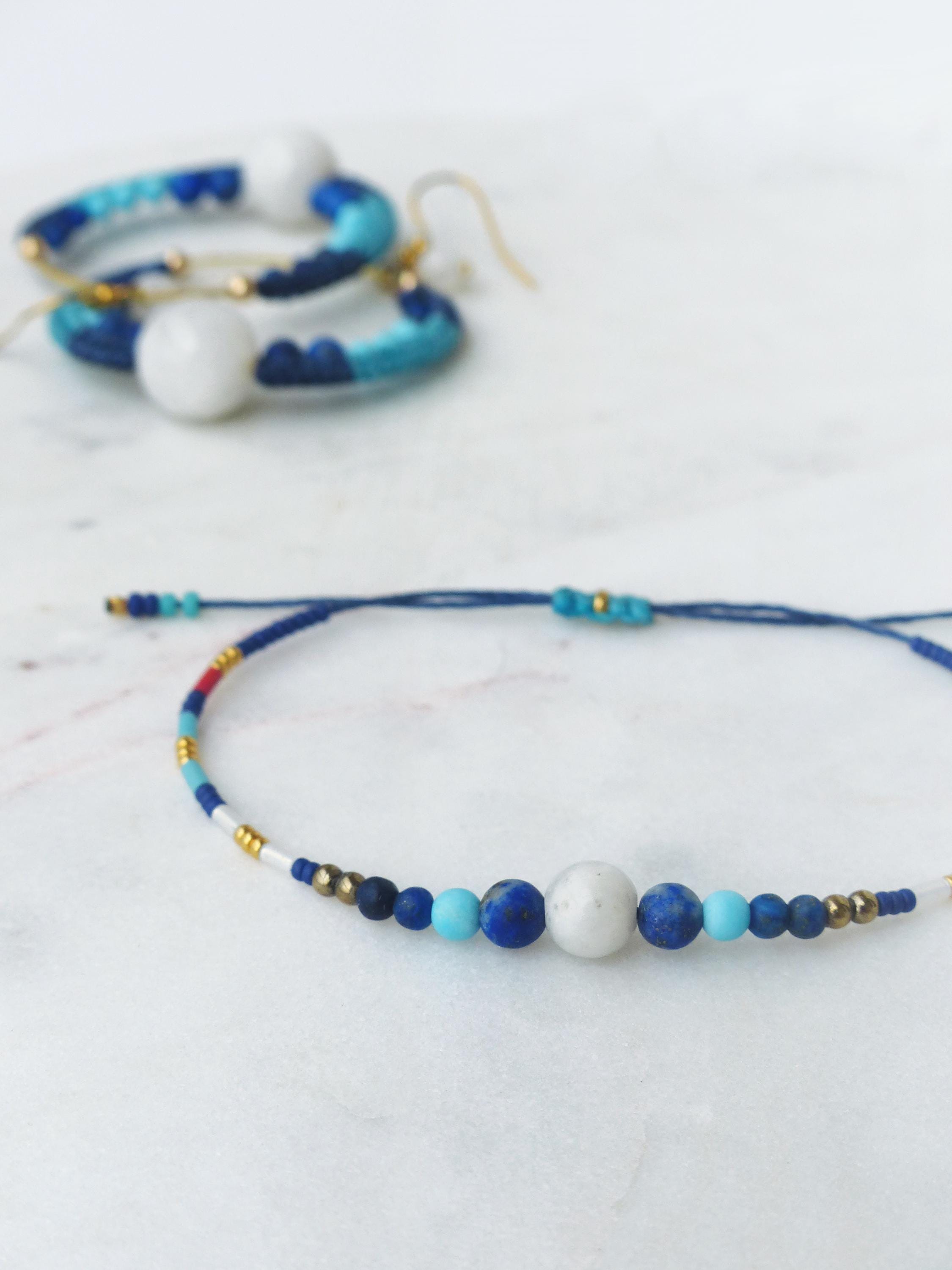 Peut inclure: Un ensemble de bracelet et boucles d'oreilles faits à la main. Le bracelet est composé d'un cordon bleu foncé orné de petites perles blanches, bleues et dorées. Les boucles d'oreilles sont de forme circulaire, avec une palette de couleurs similaire.