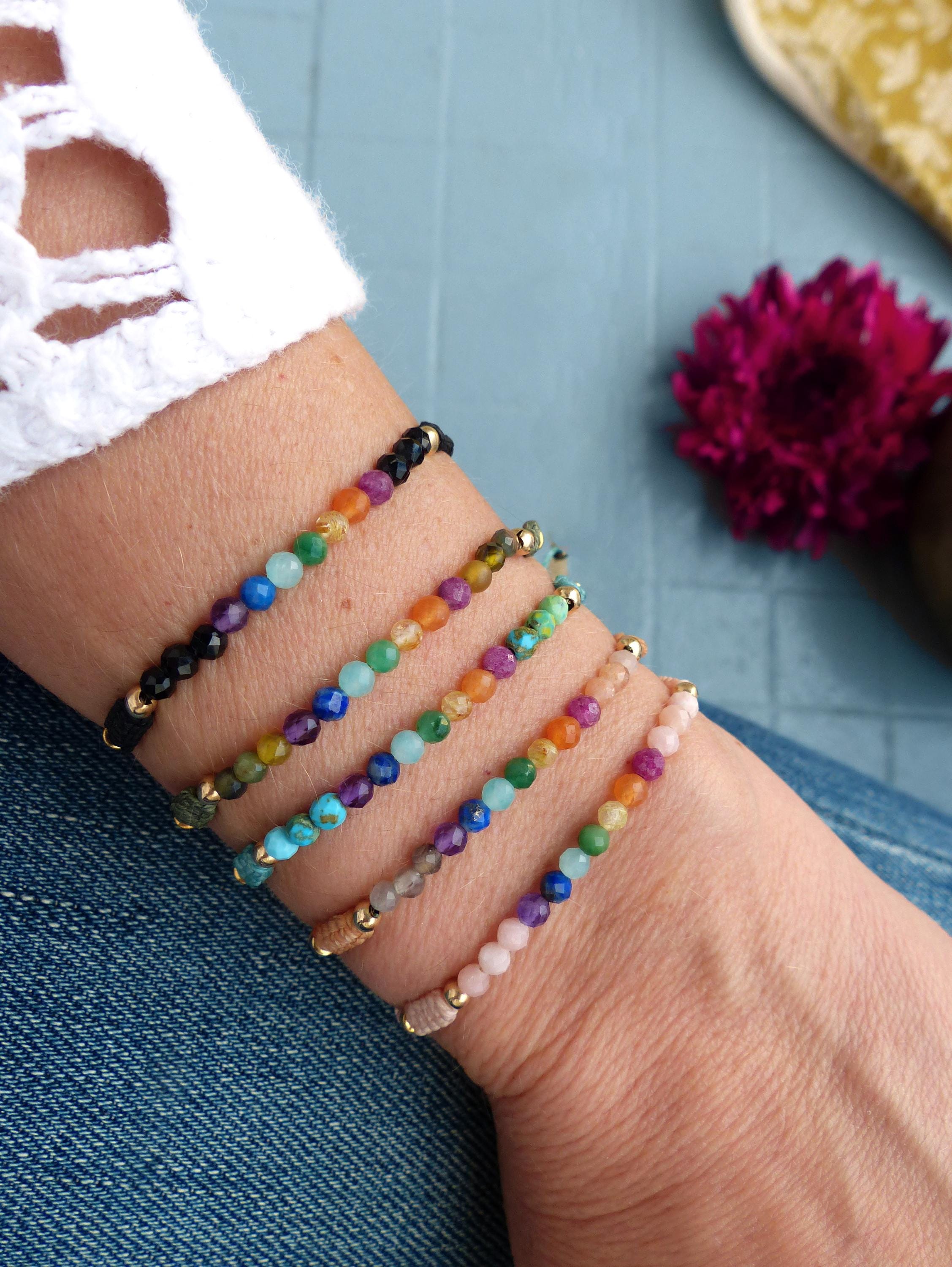 Peut inclure: Six bracelets de perles de différentes couleurs sont présentés sur un poignet. Les bracelets comportent de petites perles colorées, avec des accents dorés. Les bracelets sont sur un poignet portant un haut blanc et un jean bleu.