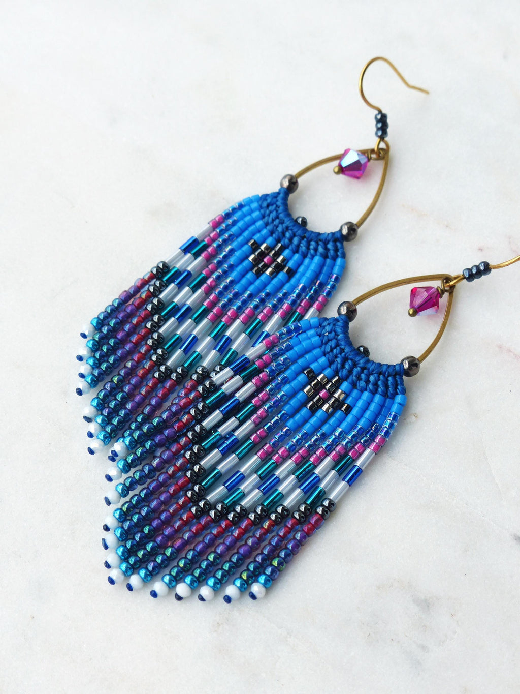 Peut inclure: Boucles d'oreilles faites à la main avec un motif géométrique vibrant. Les boucles d'oreilles présentent un jeu de couleurs bleu, rose et argenté avec une frange de perles. Elles ont des crochets couleur laiton et un petit cristal rose.