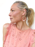 Peut inclure: Boucles d'oreilles créoles corail avec des détails dorés et une perle blanche. La personne porte un haut pêche avec des découpes florales. Un accessoire de mode.