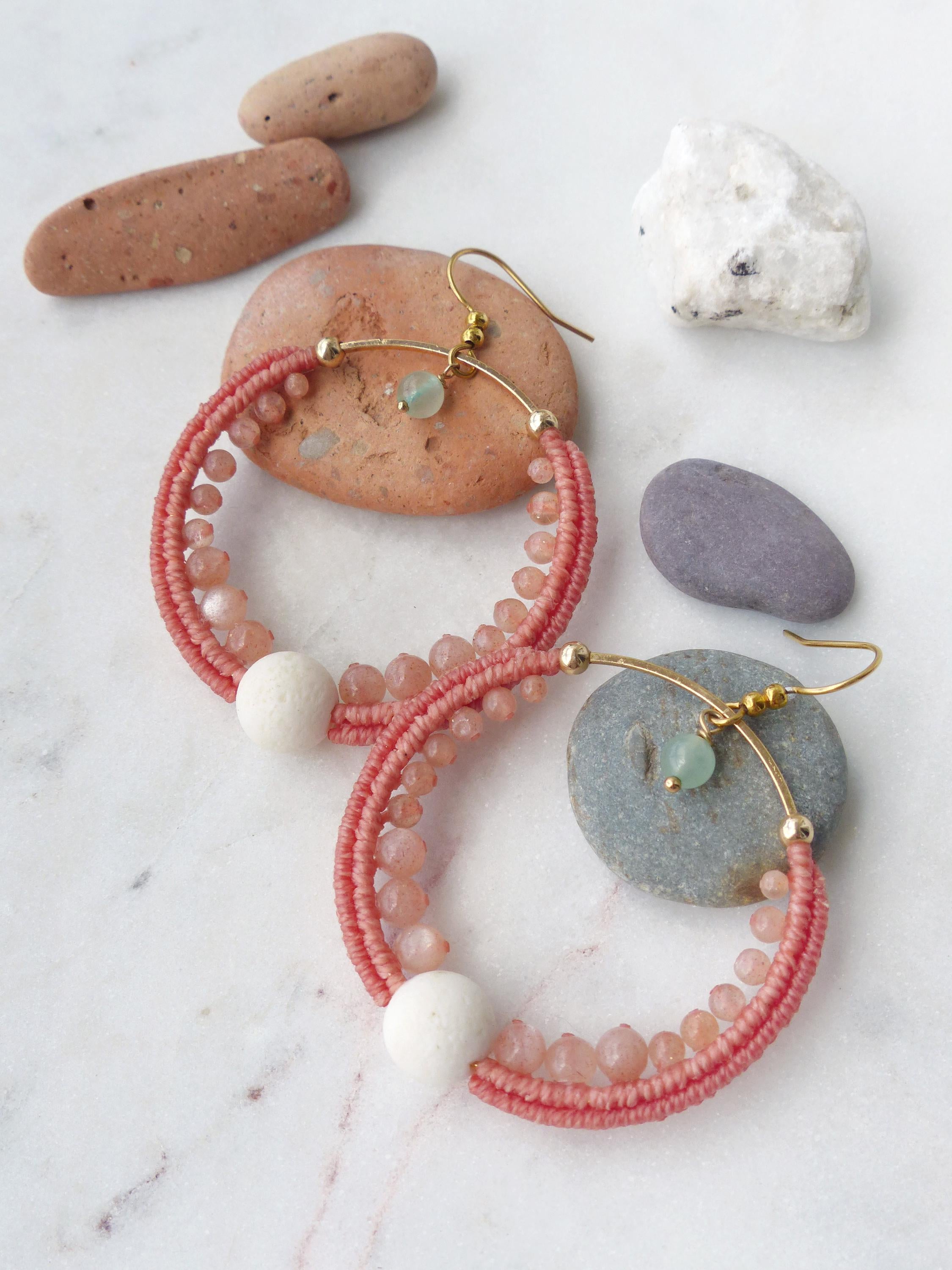 Peut inclure: Une paire de boucles d'oreilles créoles faites à la main. Elles présentent un motif tressé corail, agrémenté de petites perles roses et d'une grosse perle blanche. Les crochets dorés sont ornés d'une petite pierre verte.