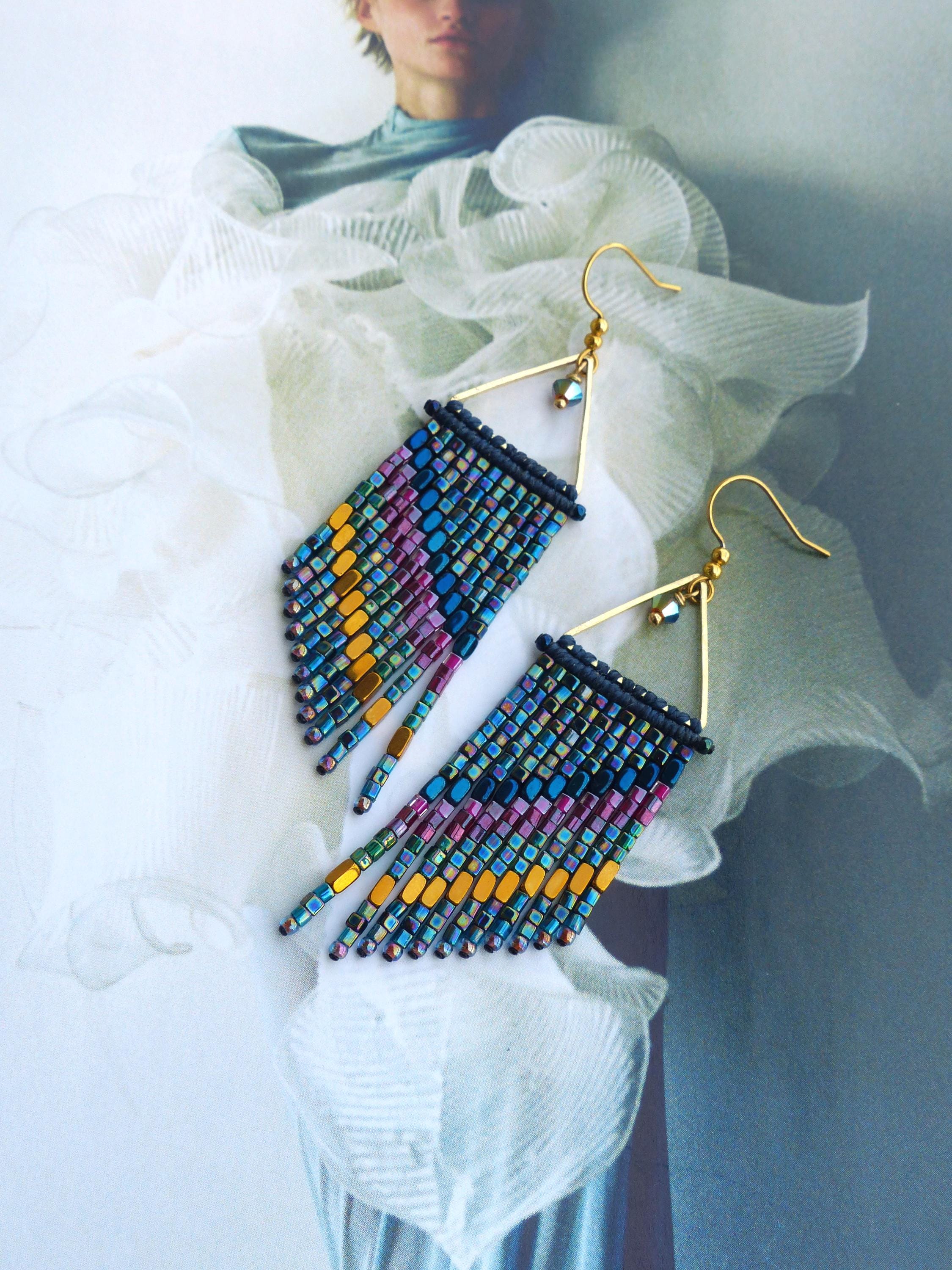 Peut inclure: Une paire de boucles d'oreilles en perles avec un cadre triangulaire doré et une frange de perles colorées. Les perles sont dans les tons de bleu, violet, jaune et vert. Les boucles d'oreilles ont des crochets d'oreilles dorés.