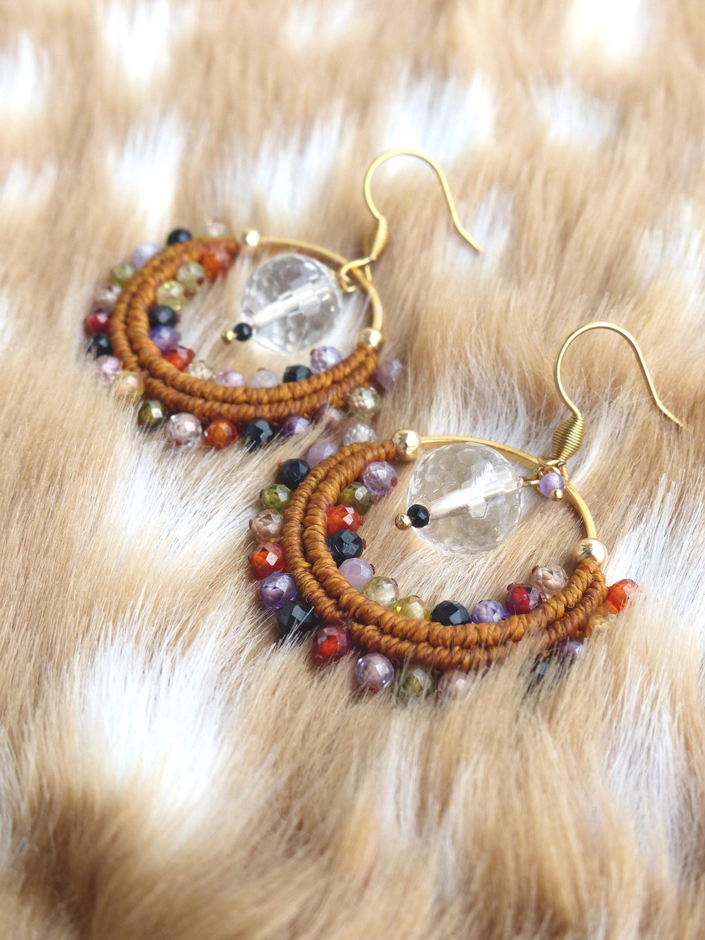 Peut inclure: Une paire de boucles d'oreilles créoles faites à la main. Les boucles d'oreilles présentent une monture en métal doré, ornée d'un fil marron tressé et d'un assortiment de perles colorées dans les tons de rouge, violet, noir et transparent. Les boucles d'oreilles sont pour oreilles percées.