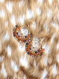 Peut inclure: Une paire de boucles d'oreilles créoles faites à la main avec des crochets dorés. Les créoles sont enveloppées de fil marron et ornées de perles colorées dans les tons de rouge, violet, orange et vert. Chaque boucle d'oreille comporte un pendentif en cristal clair et facetté.