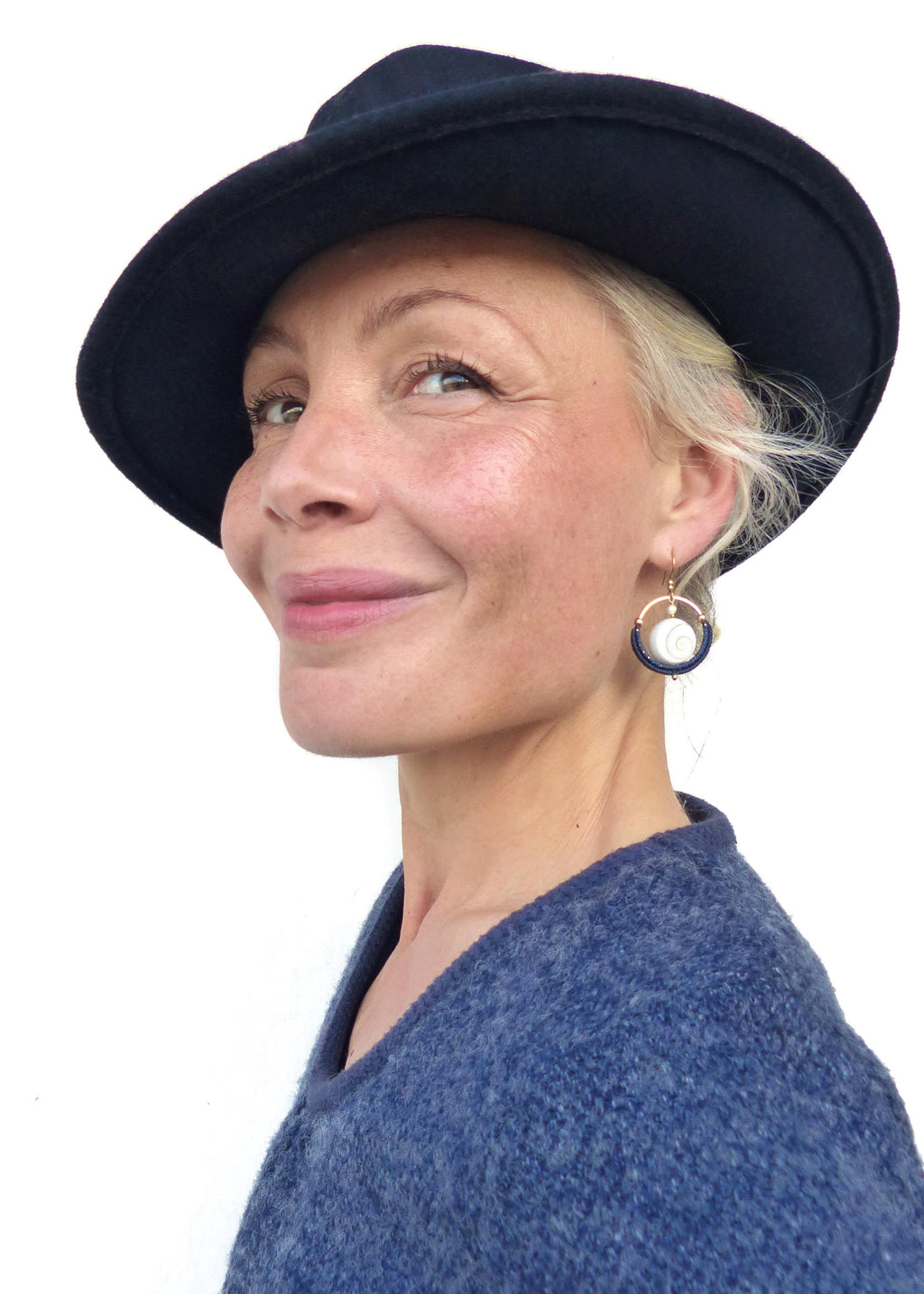 Peut inclure: Une personne portant un chapeau bleu marine et un pull bleu. Elle porte également des boucles d'oreilles dorées avec un centre blanc et une bordure bleu marine. Les boucles d'oreilles sont un accessoire unique et élégant.