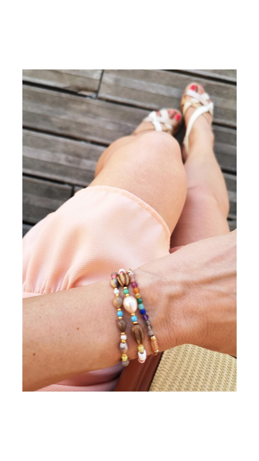 Peut inclure: Trois bracelets de perles avec une variété de perles colorées, dont des perles, des turquoises et des accents dorés. Les bracelets sont empilés sur un poignet, avec une robe pêche et des sandales blanches en arrière-plan. Accessoire de mode.