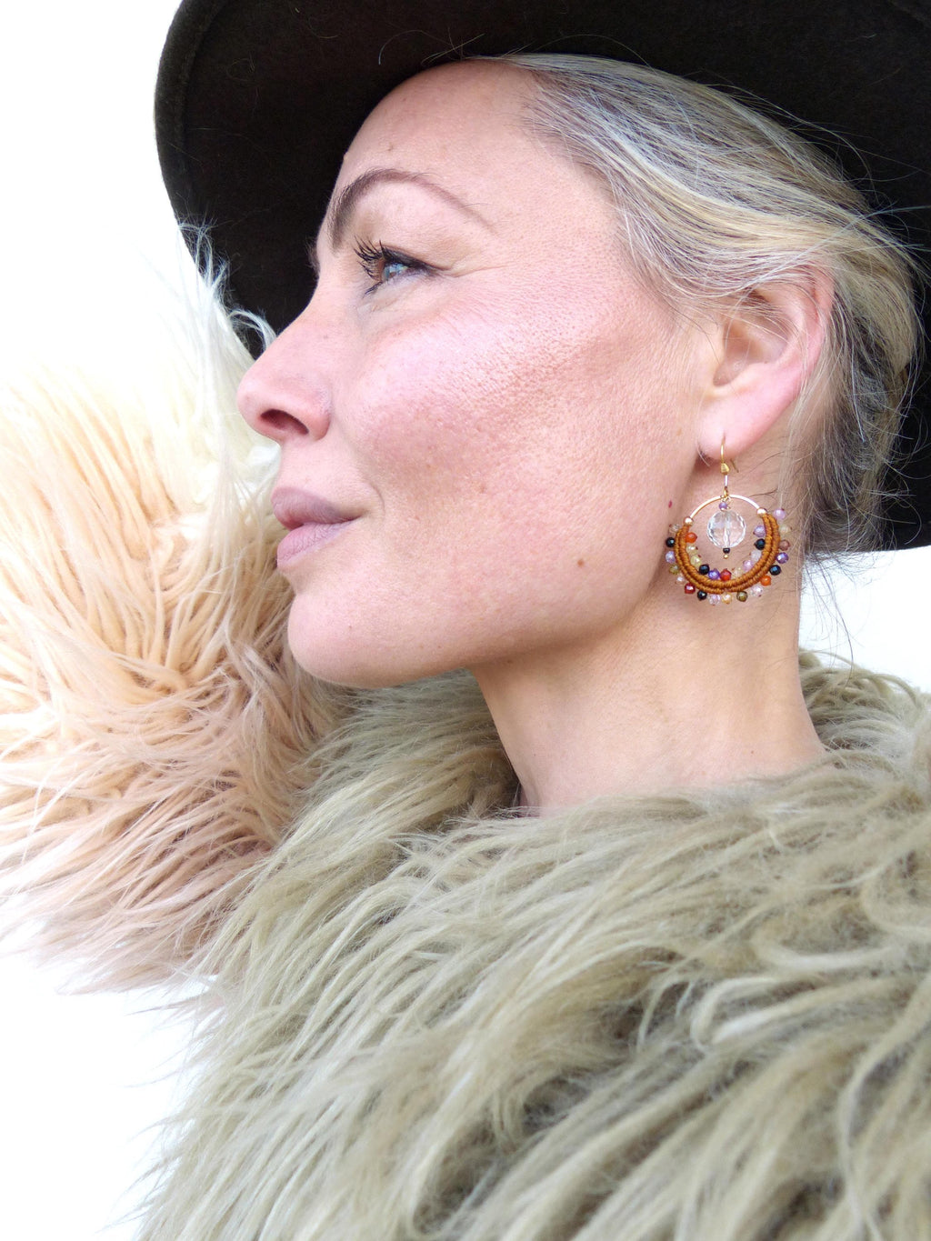 Peut inclure: Boucles d'oreilles créoles dorées avec un design circulaire, ornées de perles colorées et d'un cristal clair central. Les boucles d'oreilles sont portées avec un chapeau marron et un manteau en fausse fourrure. Un accessoire unique.
