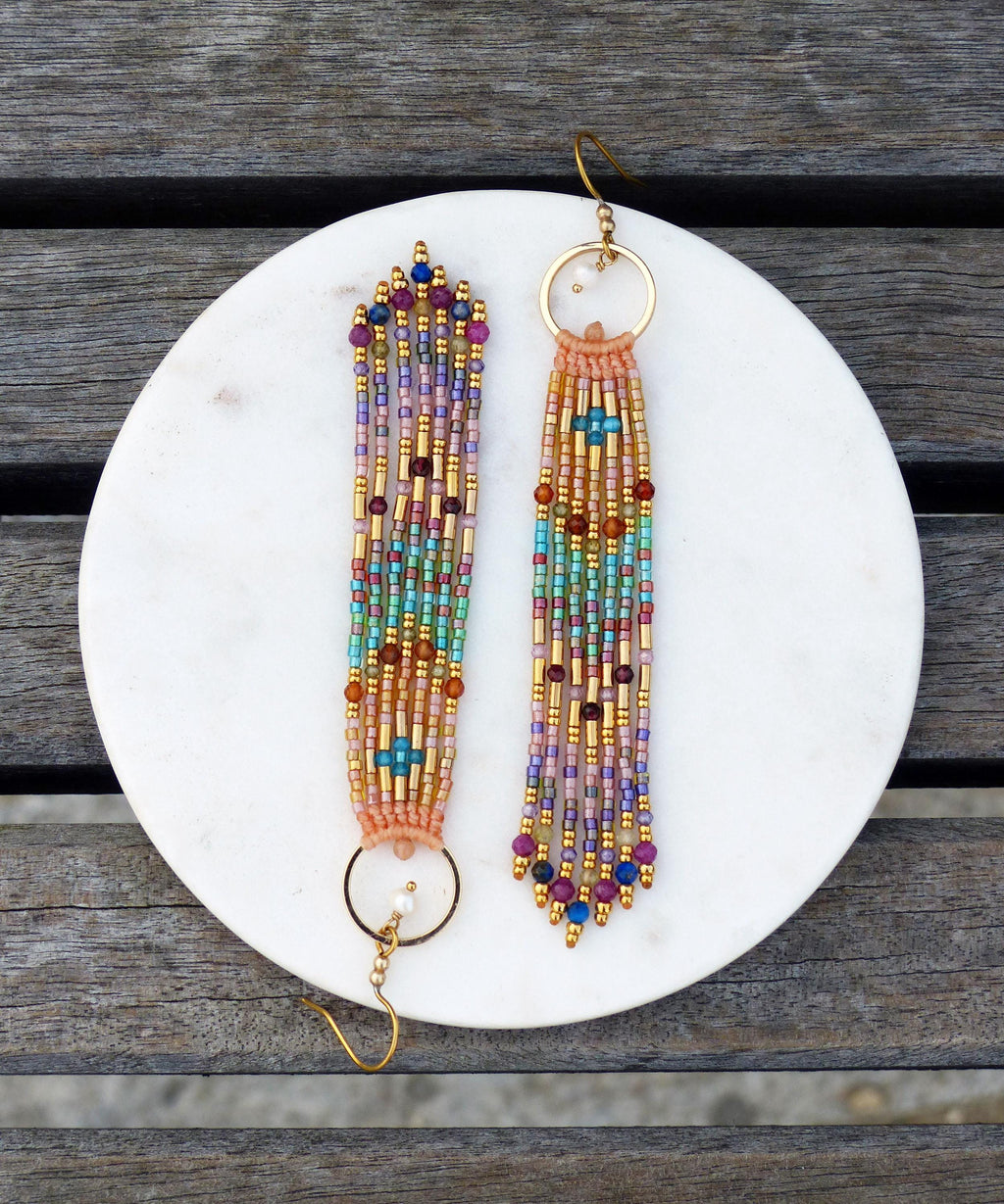 Peut inclure: Une paire de boucles d'oreilles perlées faites à la main avec un design à franges. Les boucles d'oreilles présentent un mélange de perles colorées dans des tons or, rose, violet, bleu et turquoise. Chaque boucle d'oreille a un cercle doré et une frange perlée.