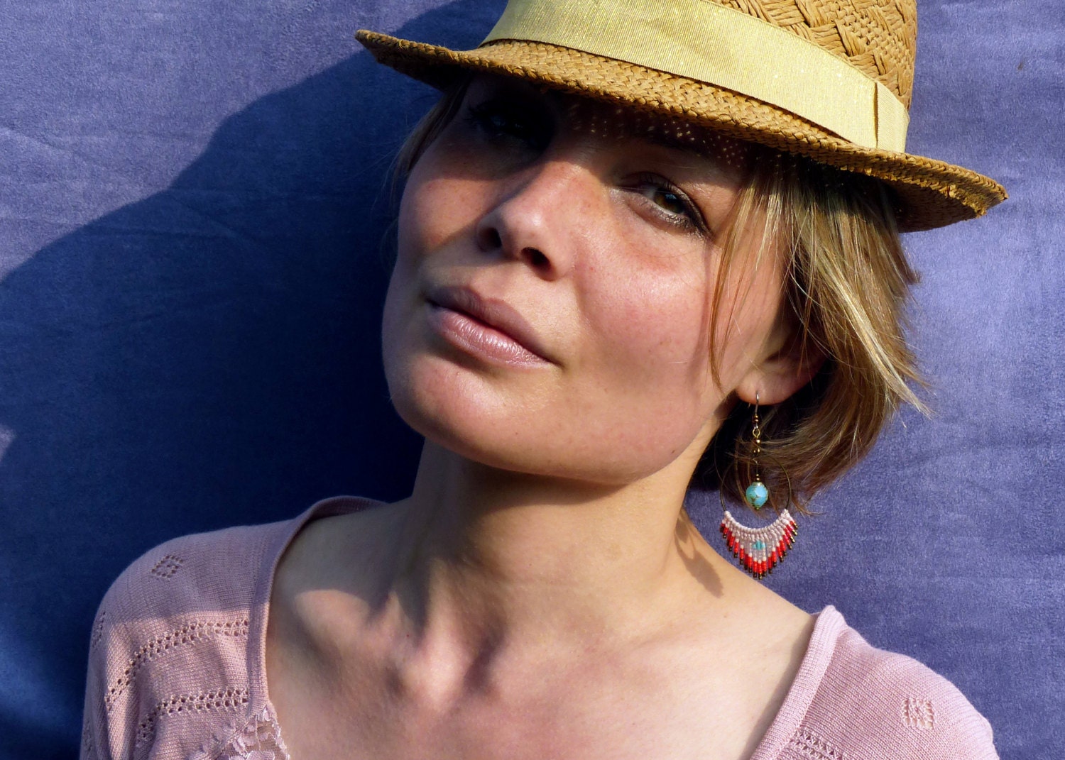 Peut inclure: Une femme portant un chapeau fedora brun avec un bandeau brun clair et un haut en tricot rose. Elle porte une boucle d'oreille en perles turquoise et rouge.