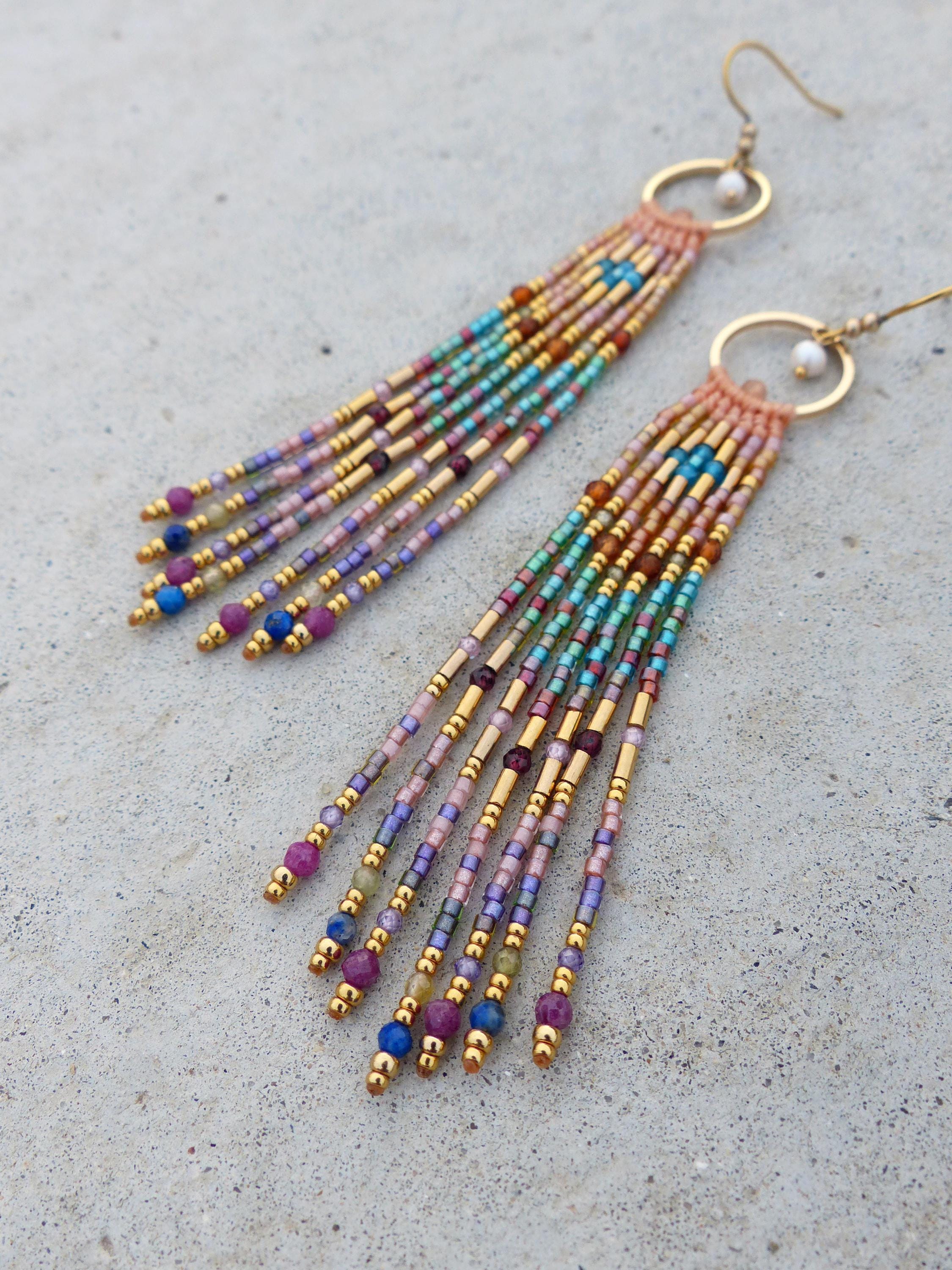 Peut inclure: Boucles d'oreilles faites à la main avec un design à franges. Les boucles d'oreilles présentent un mélange de perles colorées dans les tons de rose, de bleu, de vert et d'or. Les boucles d'oreilles ont des accents métalliques dorés et une fermeture à crochet.