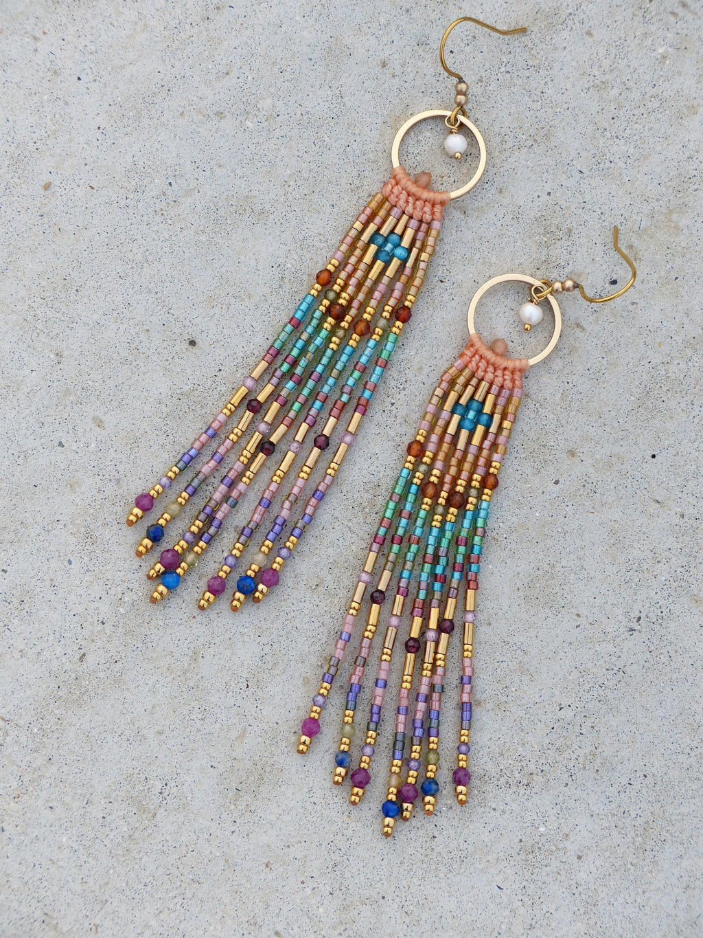 Peut inclure: Une paire de boucles d'oreilles en perles avec des cerceaux et des crochets d'oreilles dorés. Les boucles d'oreilles présentent une frange de perles colorées dans les tons de rose, bleu, vert, violet et or. Les boucles d'oreilles ont un style bohème.