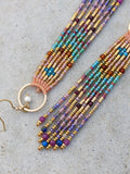 Peut inclure: Gros plan sur deux boucles d'oreilles perlées. Les boucles d'oreilles présentent une variété de perles colorées dans les tons rose, bleu, violet et or. Les boucles d'oreilles ont un design à franges et sont attachées à des cerceaux dorés.