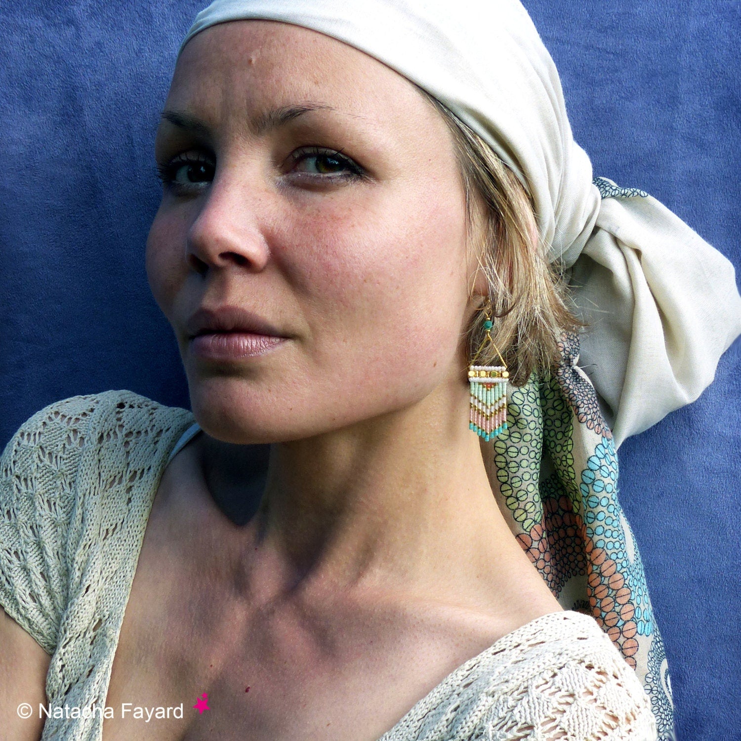Peut inclure: Une femme portant un foulard blanc et un foulard à motifs vert clair et blanc noué autour du cou. Elle porte un haut en crochet blanc et des boucles d'oreilles en perles dorées et turquoise.