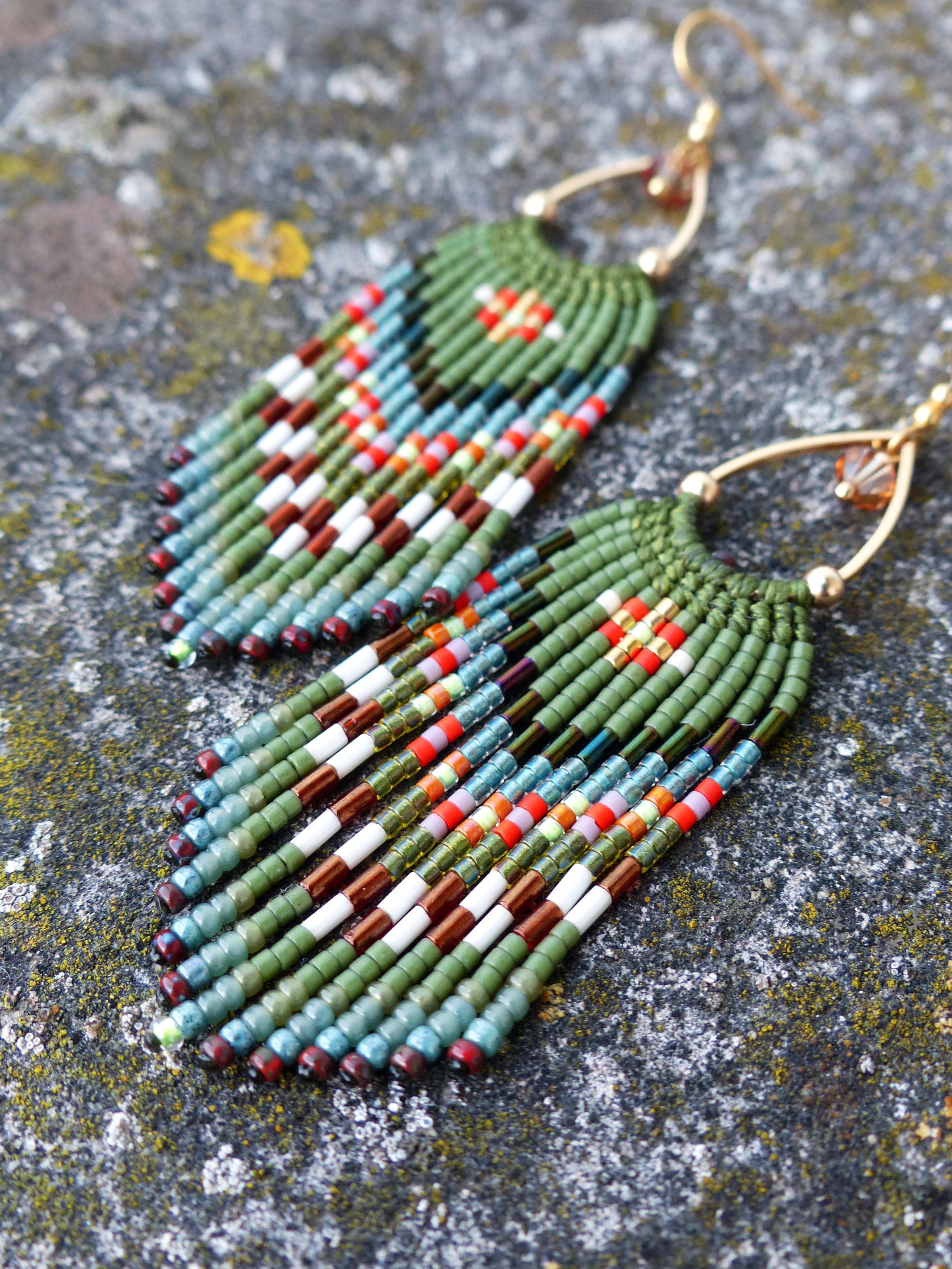 Peut inclure: Une paire de boucles d'oreilles perlées faites à la main. Les boucles d'oreilles présentent un dessus vert perlé avec une frange de perles colorées dans les tons de rouge, blanc, marron et bleu. Les boucles d'oreilles ont des crochets d'oreilles dorés.