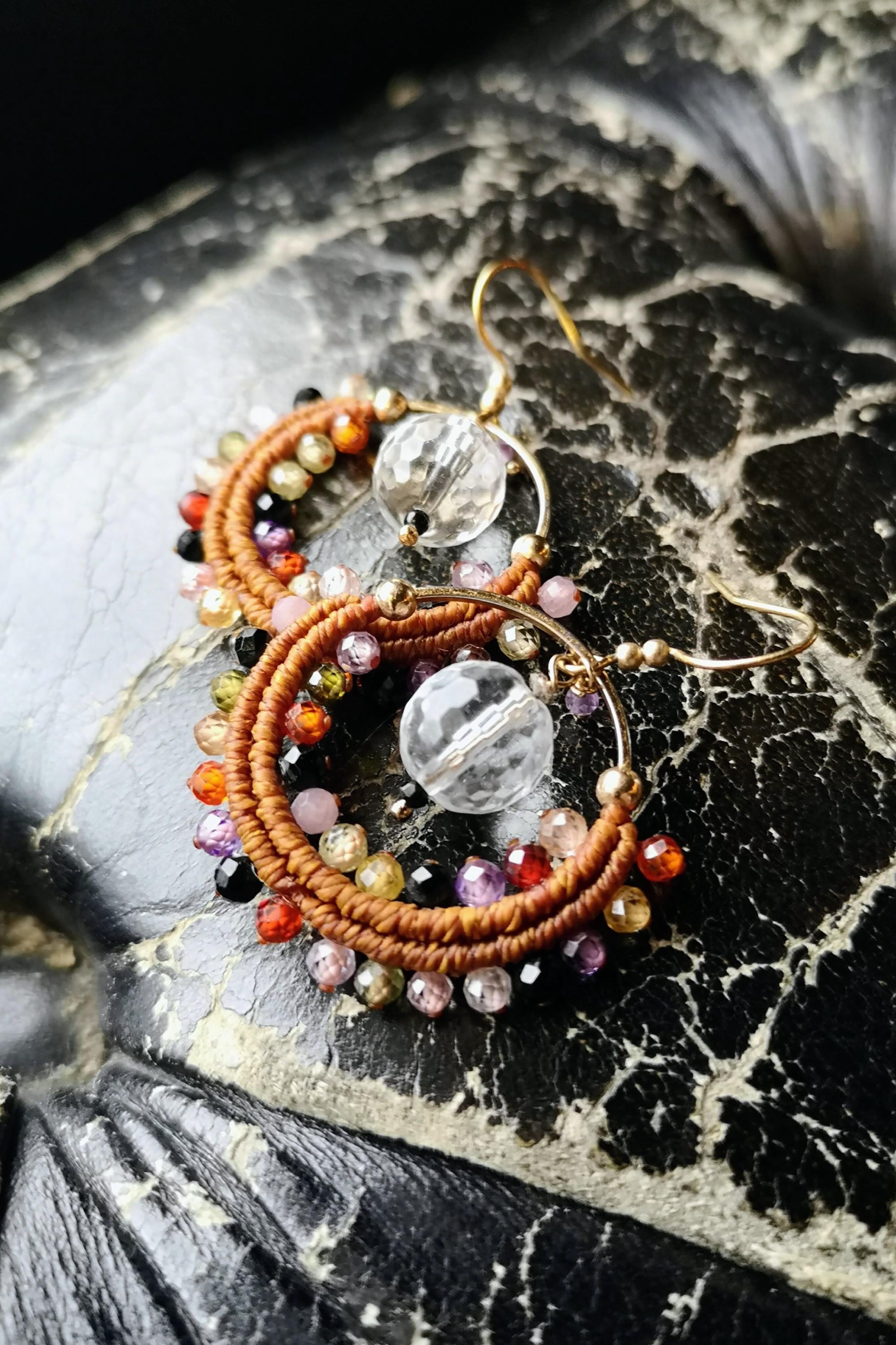 Peut inclure: Boucles d'oreilles créoles faites à la main avec un design macramé. Les boucles d'oreilles présentent une variété de perles colorées, dont des perles facettées transparentes et des perles plus petites dans les tons de rouge, orange, jaune, rose, violet et noir. Les créoles sont dorées.