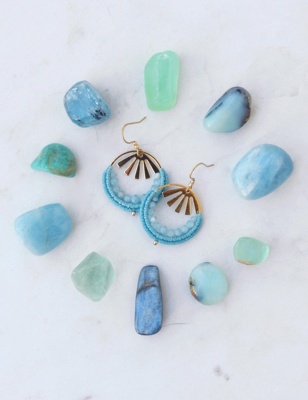 Peut inclure: Boucles d'oreilles créoles turquoise ornées de perles, avec des détails dorés en forme de soleil, entourées de pierres précieuses bleues et vertes sur une surface blanche. Bijoux faits main.