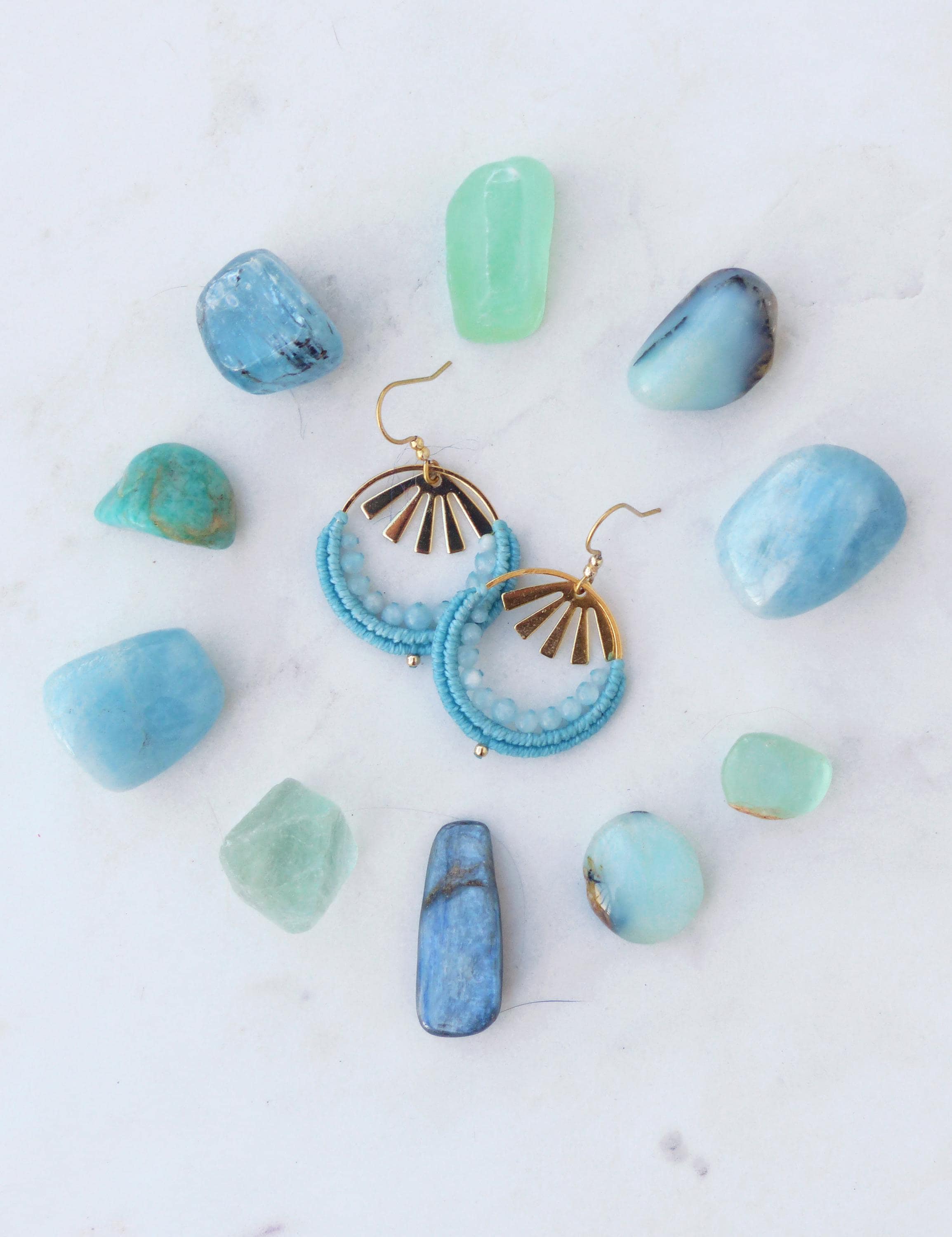 Peut inclure: Boucles d'oreilles créoles turquoise ornées de perles, avec des détails dorés en forme de soleil, entourées de pierres précieuses bleues et vertes sur une surface blanche. Bijoux faits main.