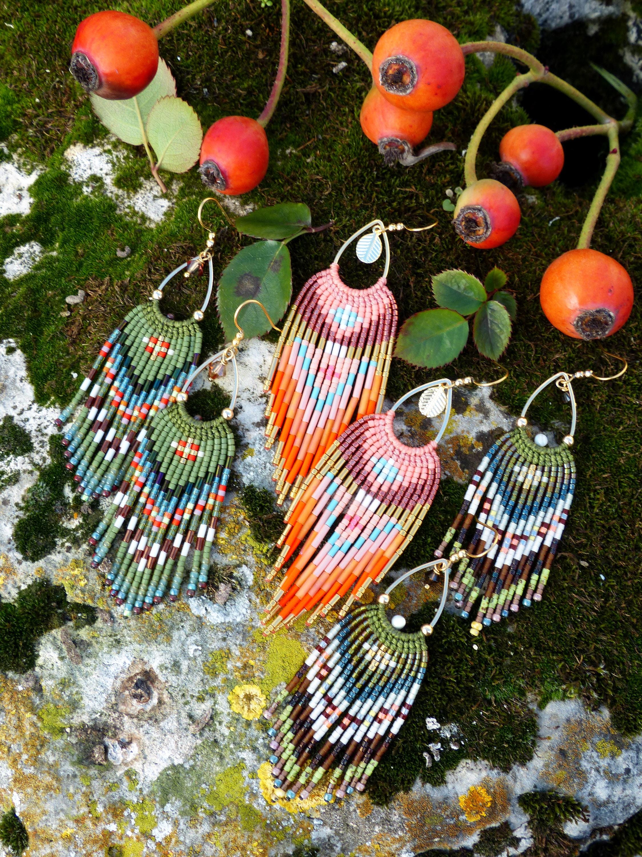 Peut inclure: Gros plan sur plusieurs boucles d'oreilles à franges perlées de différentes couleurs, dont le vert, l'orange, le rose et le marron. Les boucles d'oreilles sont présentées sur une surface moussue avec des baies rouges et des feuilles vertes.