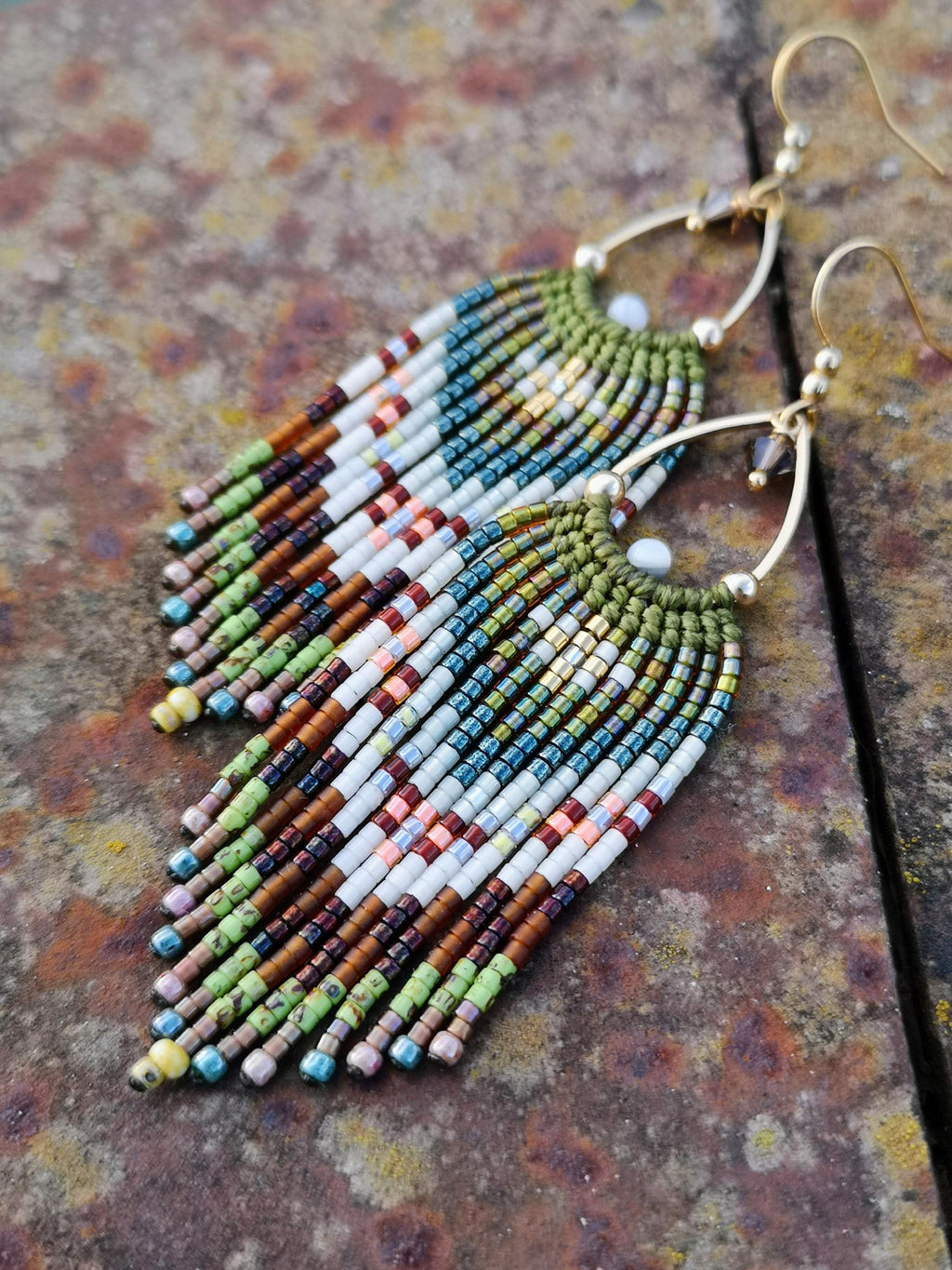 Peut inclure: Boucles d'oreilles faites à la main avec un motif de franges. Les boucles d'oreilles présentent un fil d'oreille doré et un motif de perles blanches, marron, vertes, bleues et roses. Les boucles d'oreilles sont de style bohème.