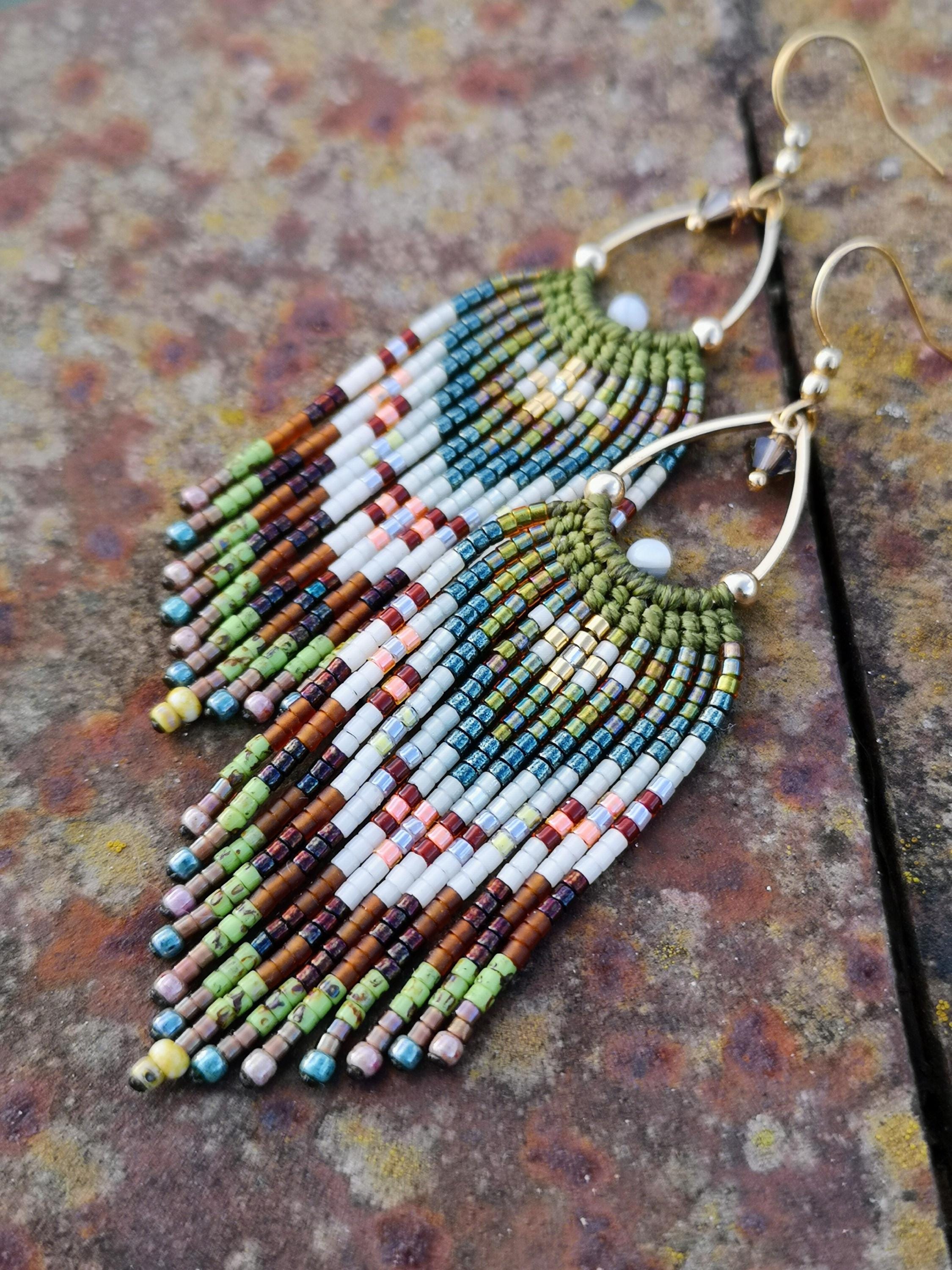 Peut inclure: Boucles d'oreilles faites à la main avec un motif de franges. Les boucles d'oreilles présentent un fil d'oreille doré et un motif de perles blanches, marron, vertes, bleues et roses. Les boucles d'oreilles sont de style bohème.