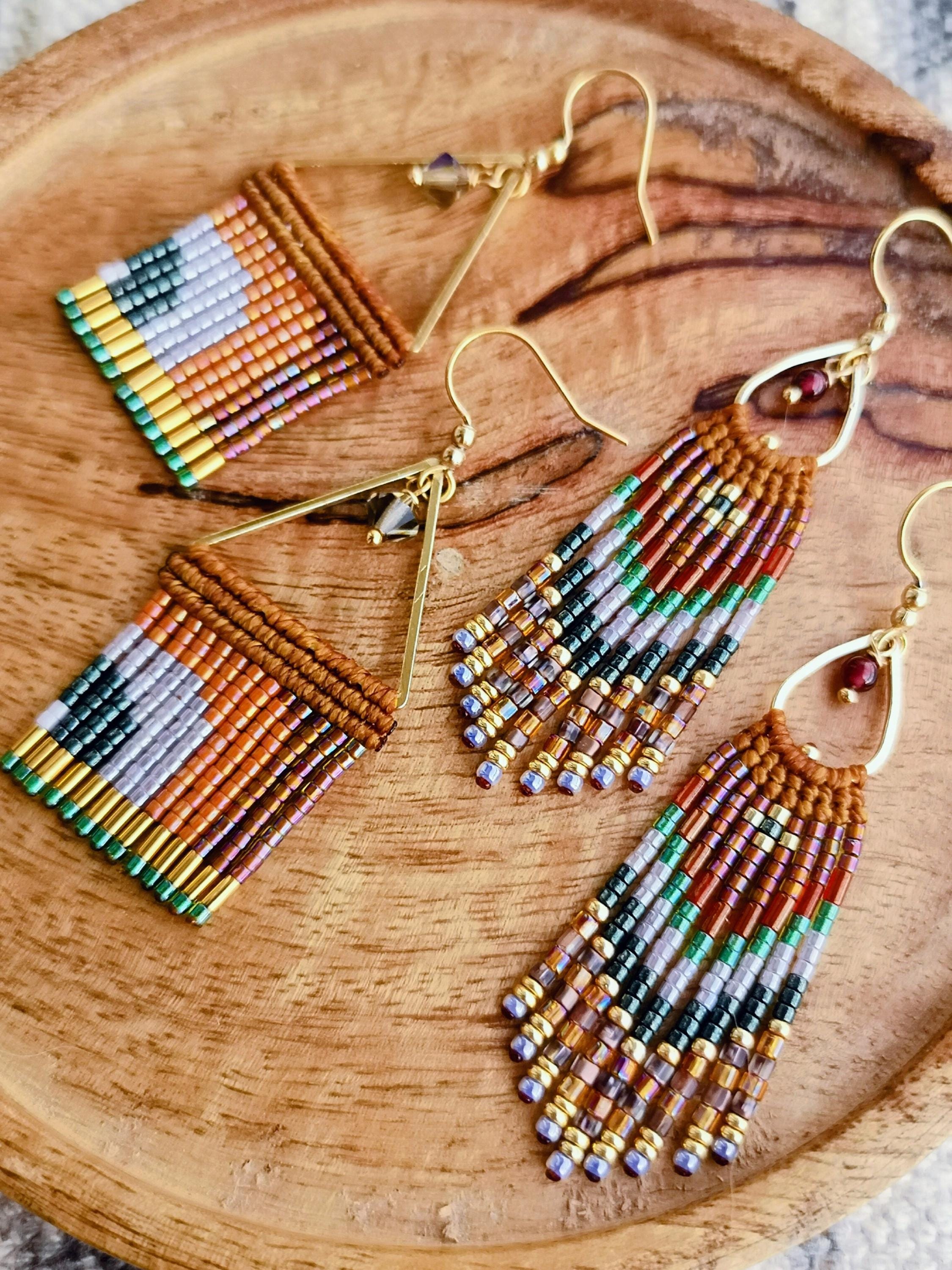 Peut inclure: Deux paires de boucles d'oreilles faites à la main avec un motif géométrique. Les boucles d'oreilles présentent un motif tissé de perles colorées dans les tons de marron, orange, vert, noir et violet. Les boucles d'oreilles ont des crochets dorés et sont présentées sur un plateau en bois.