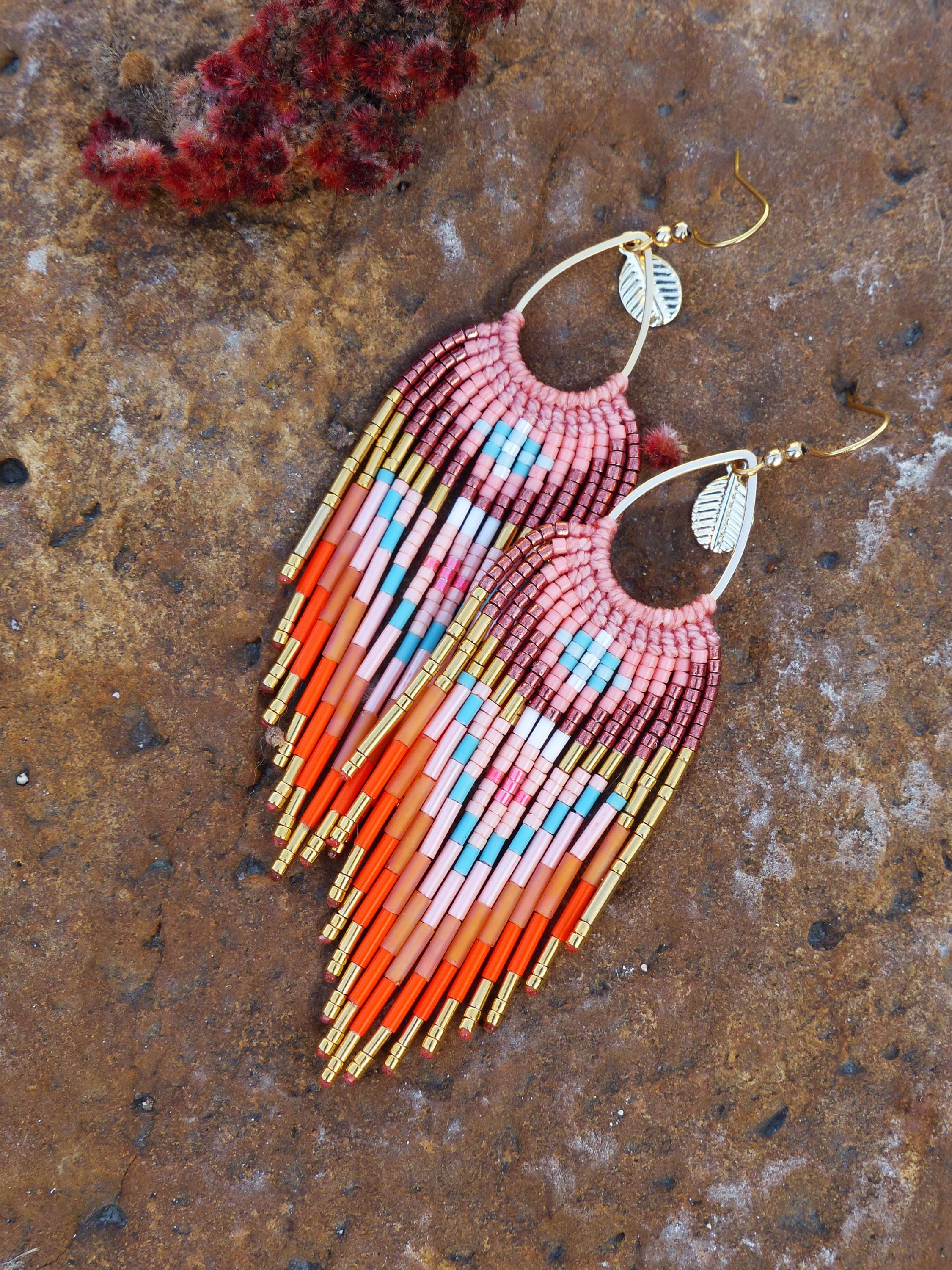 Peut inclure: Boucles d'oreilles en perles faites à la main avec un design à franges. Les boucles d'oreilles présentent une palette de couleurs rose, orange, bleu et or. Les boucles d'oreilles ont une forme de goutte d'eau avec un crochet doré et un petit charme en forme de feuille.