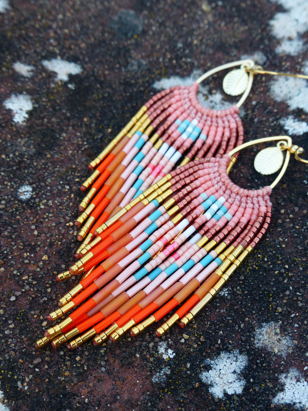 Peut inclure: Une paire de boucles d'oreilles en perles faites à la main avec un design à franges. Les boucles d'oreilles présentent une combinaison de perles roses, oranges, bleues et dorées. Les boucles d'oreilles sont suspendues à des crochets d'oreilles dorés.