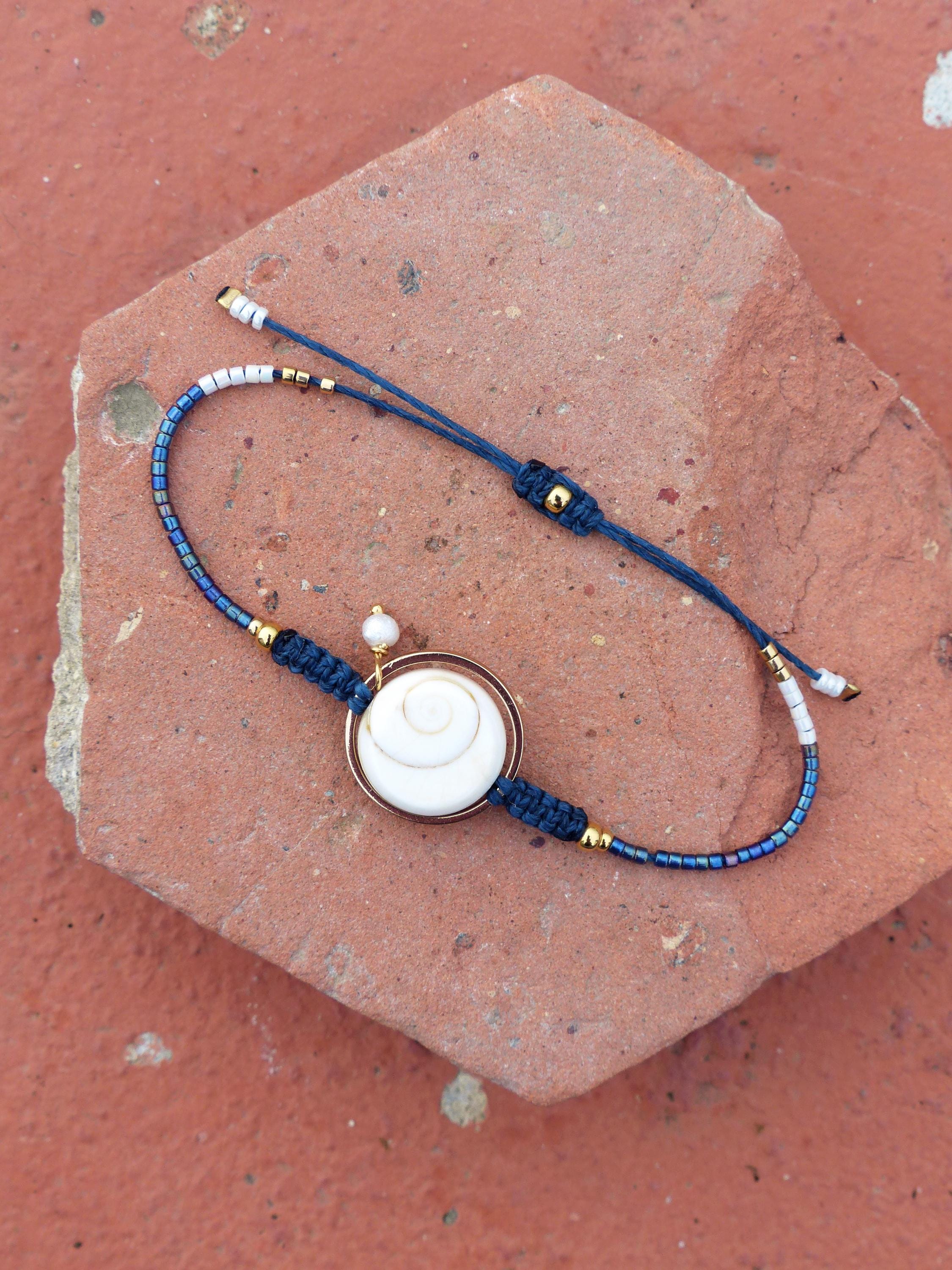 Peut inclure: Bracelet fait à la main avec un pendentif coquillage blanc dans un cadre doré. Le bracelet en cordon bleu marine a des perles et des accents dorés. Le design réglable comprend des perles de rocaille blanches et bleues.