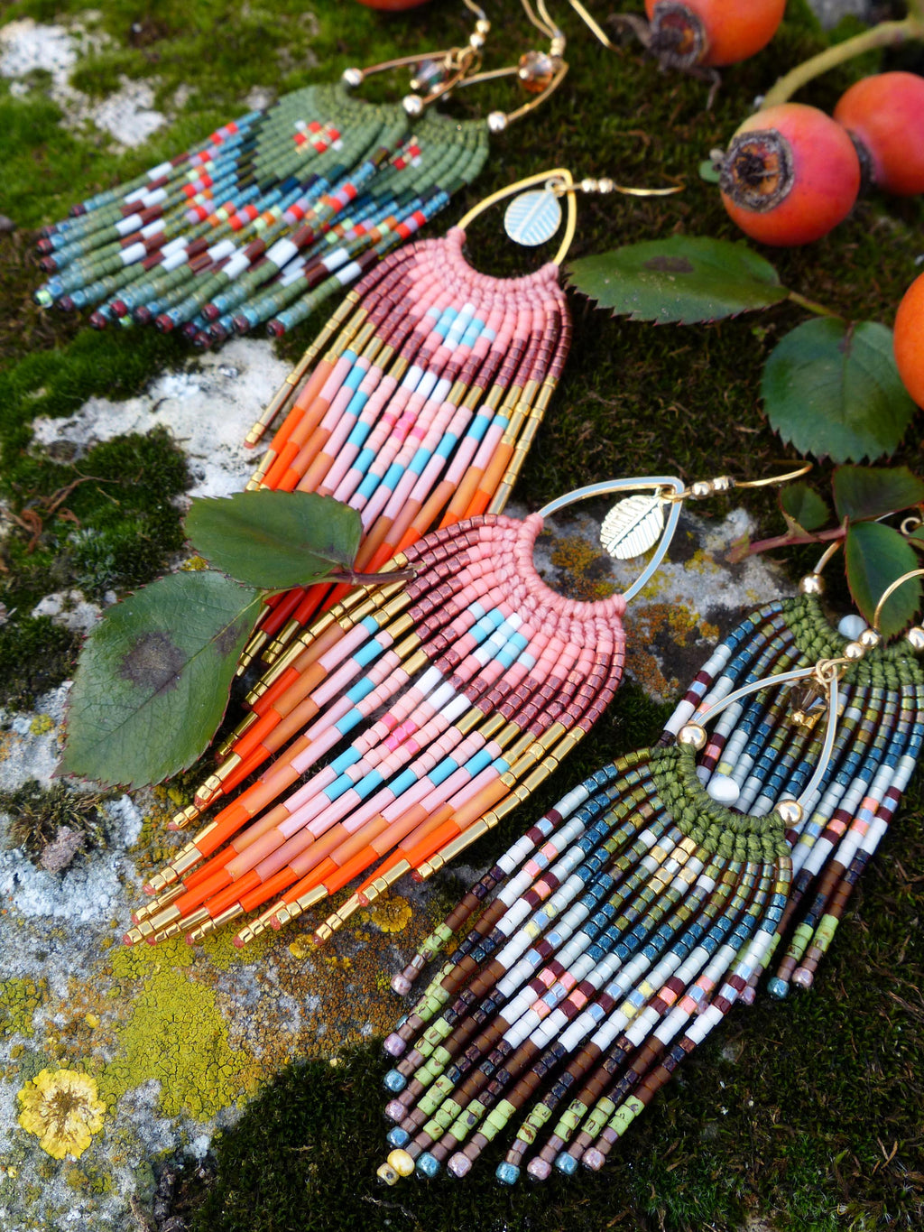 Peut inclure: Gros plan sur quatre paires de boucles d'oreilles perlées faites à la main. Les boucles d'oreilles présentent une variété de couleurs, notamment rose, orange, vert, bleu et or. Elles sont disposées sur une surface moussue avec des cynorhodons et des feuilles.