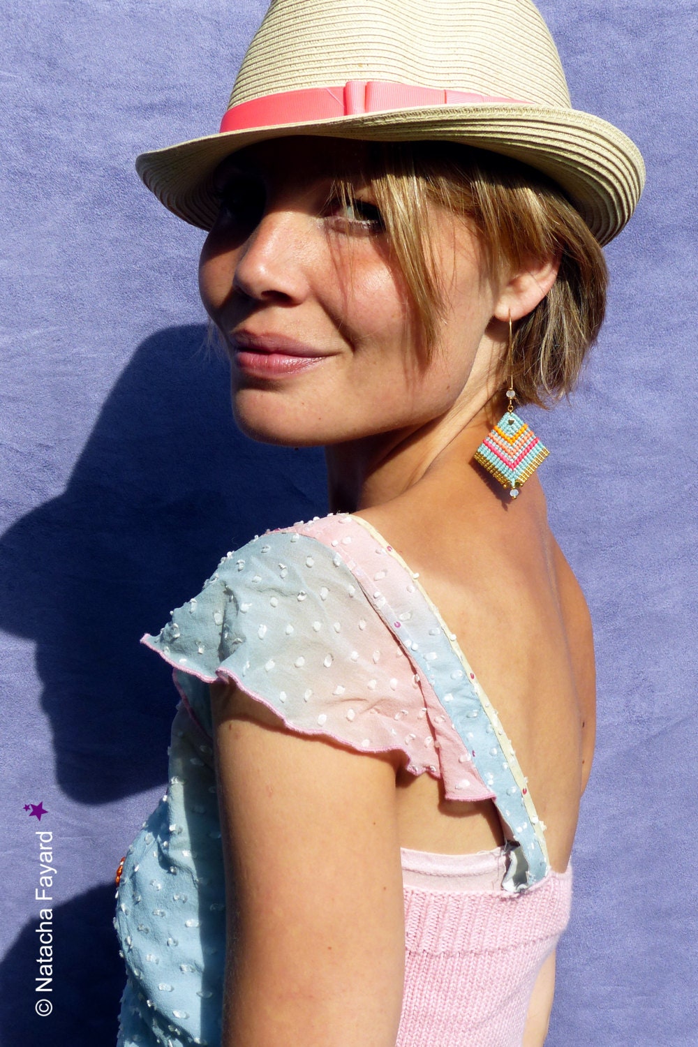 Peut inclure: Une femme portant un chapeau de paille avec un ruban rose, une robe à pois bleu clair et rose et des boucles d'oreilles en perles turquoise et jaunes. 