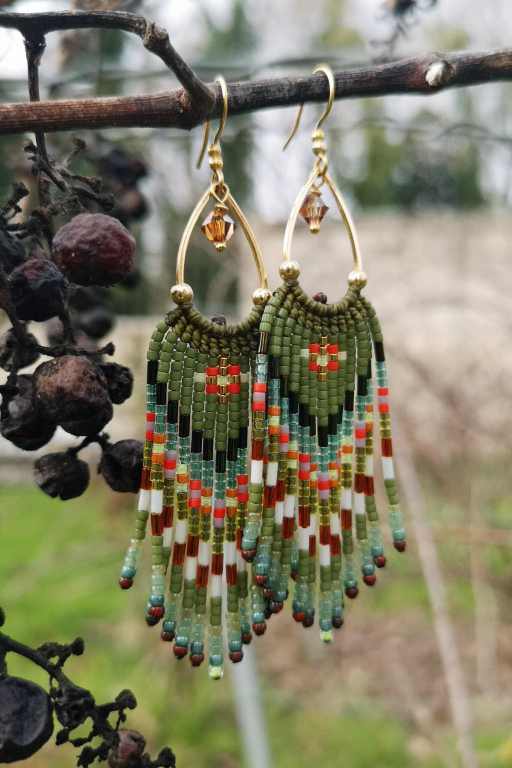 Peut inclure: Boucles d'oreilles perlées faites à la main avec un crochet doré. Les boucles d'oreilles présentent une base perlée verte avec un motif géométrique rouge, blanc, noir et orange. La frange est faite de perles colorées.
